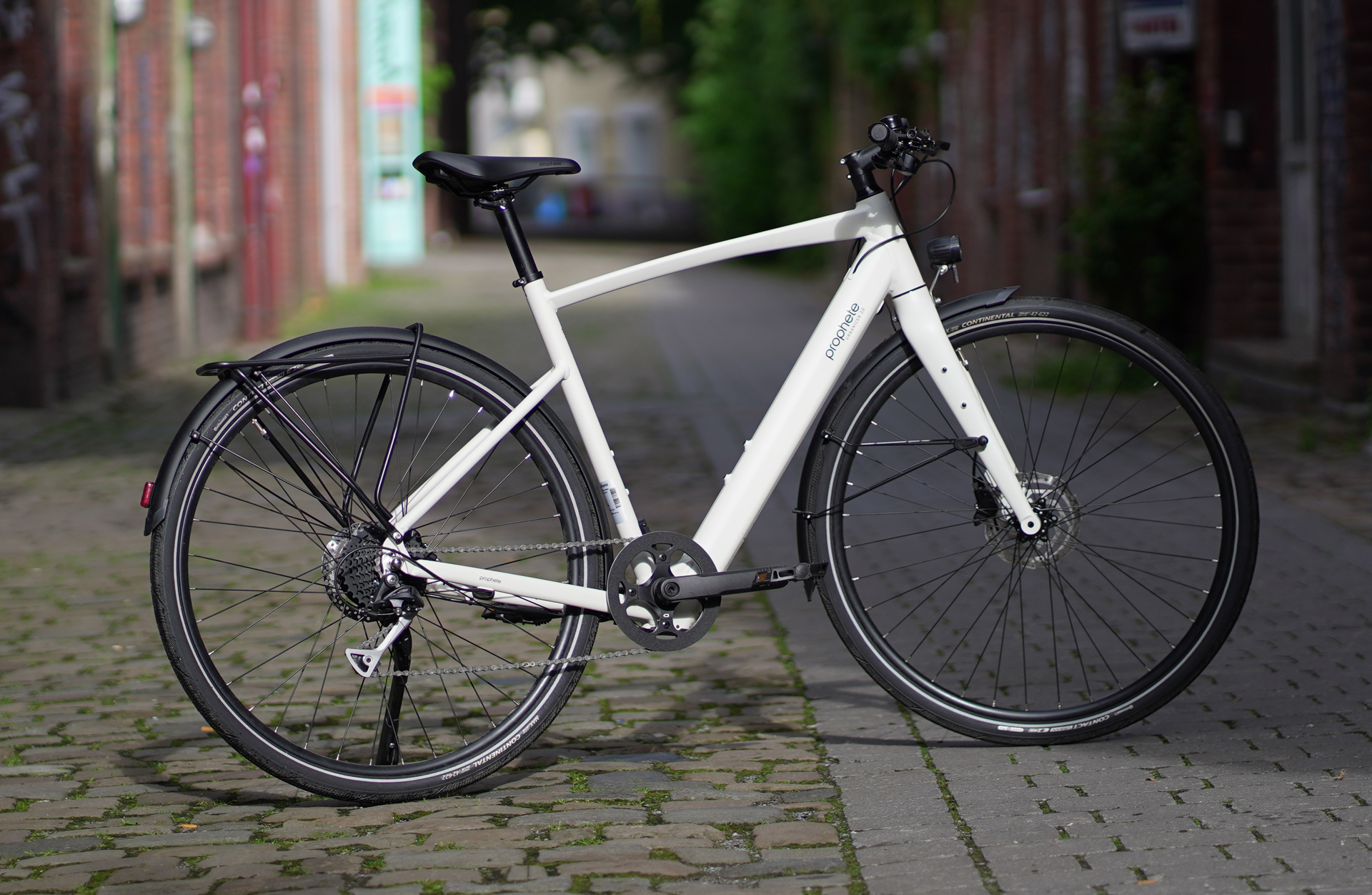 Ein weißes E-Bike mit Gepäckträger steht auf einem Kopfsteinpflasterweg.