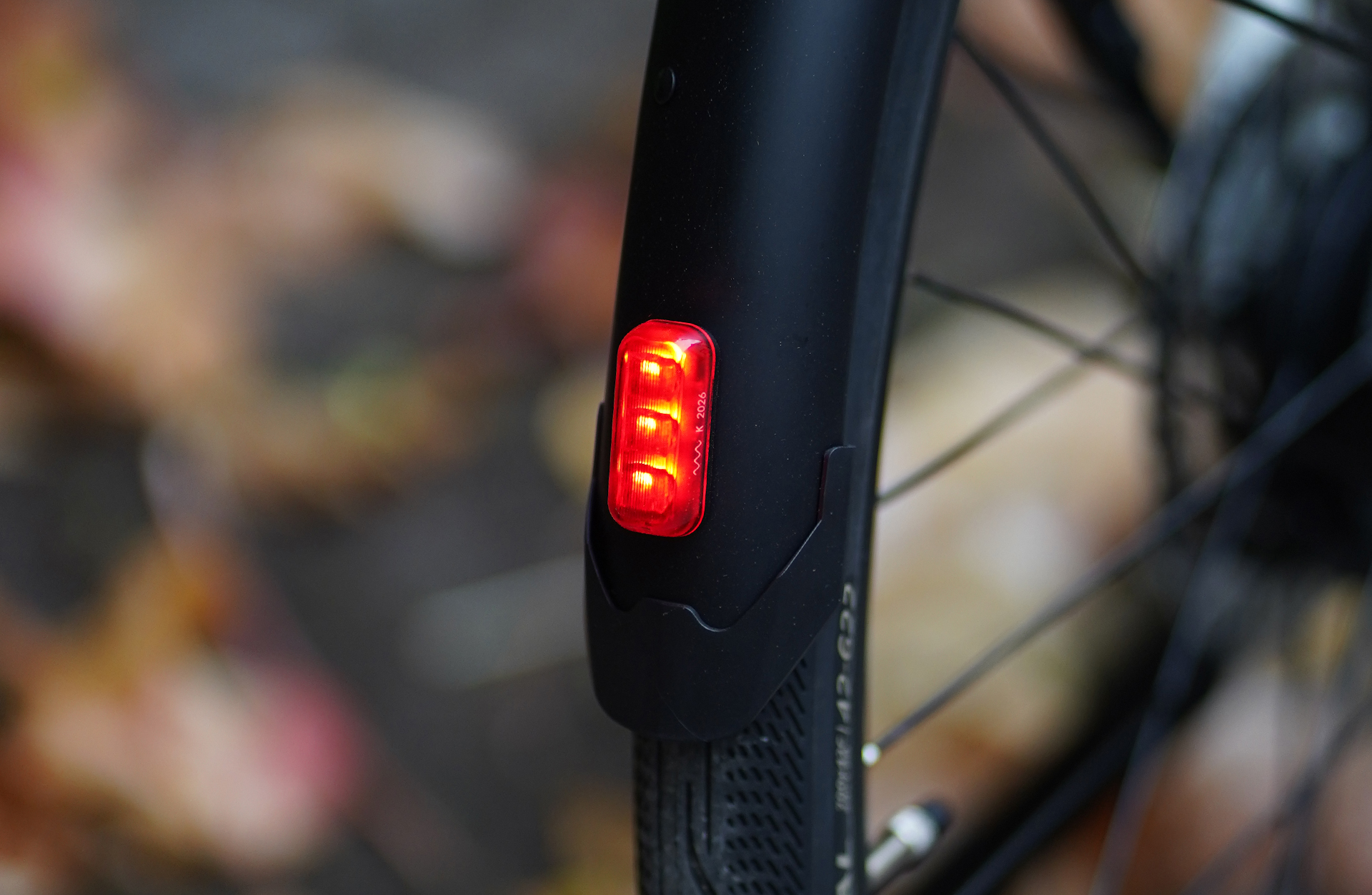 Ein rotes Rücklicht leuchtet auf dem schwarzen Schutzblech eines Fahrrads.