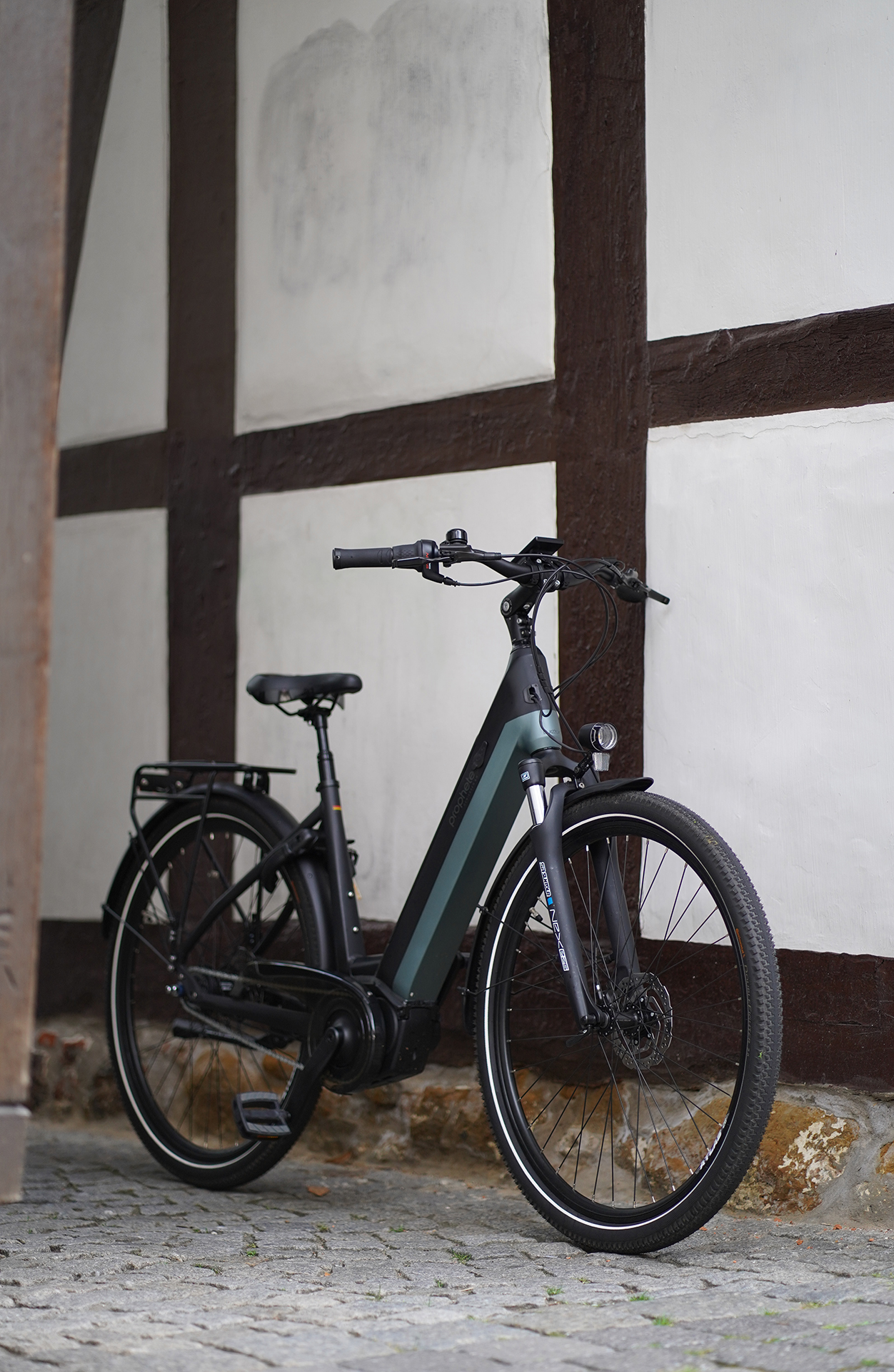 Ein Elektrofahrrad steht vor einem Gebäude mit hellfarbiger Wand und dunkelbraunen Balken.