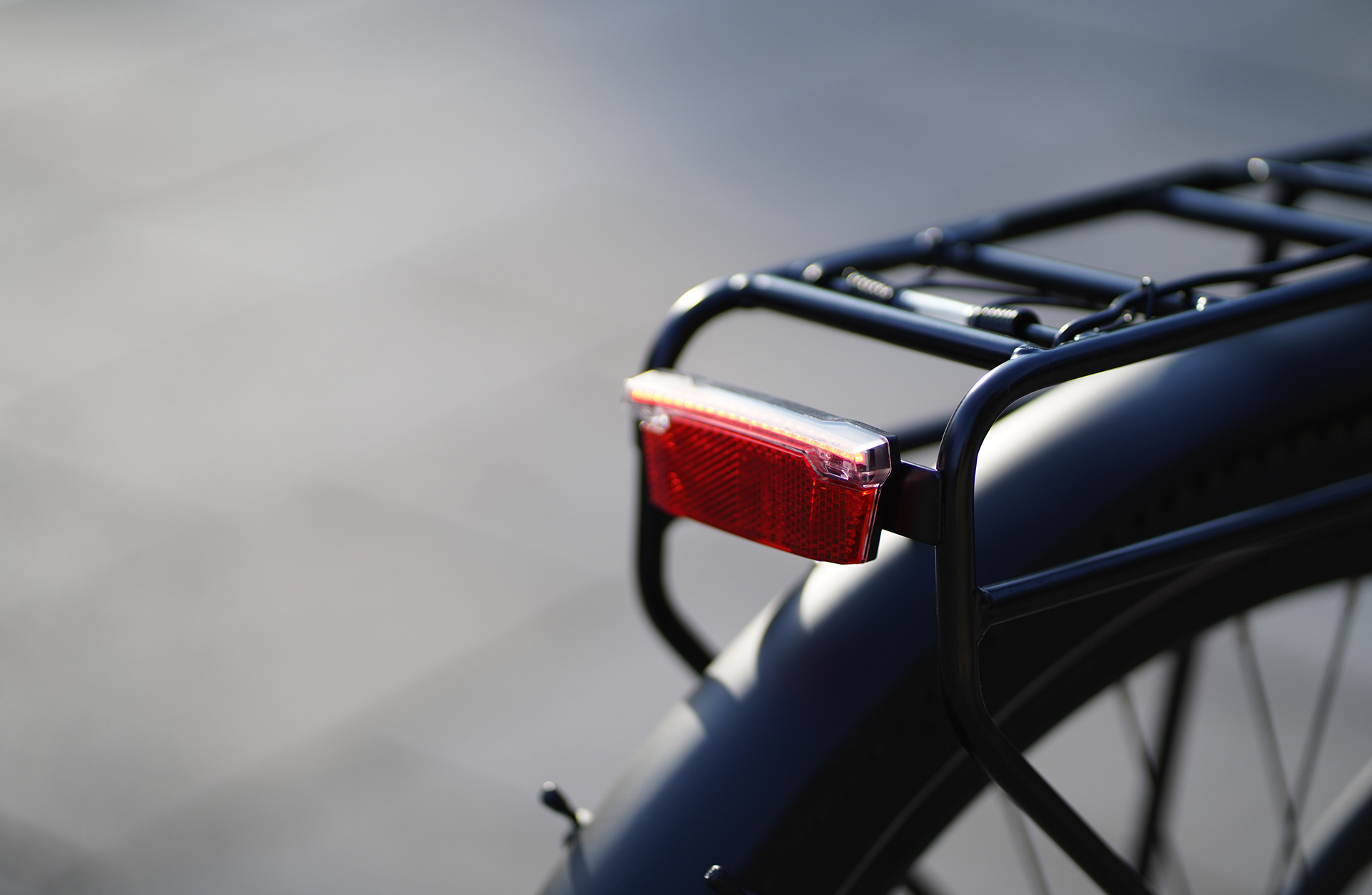 Nahaufnahme des Hecks eines Elektrofahrrads, mit einem roten Reflektor am schwarzen Gepäckträger.