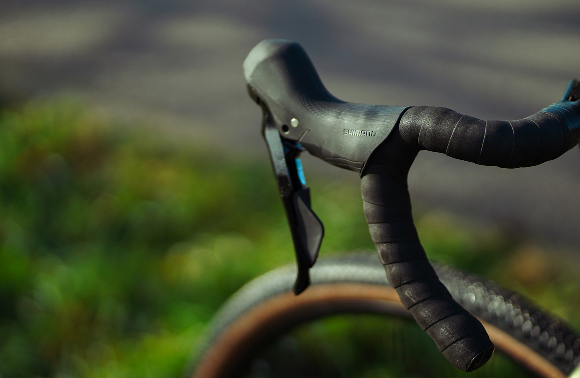 Schwarzer Fahrradlenker mit Shimano-Schalthebel vor unscharfem grünen Hintergrund.