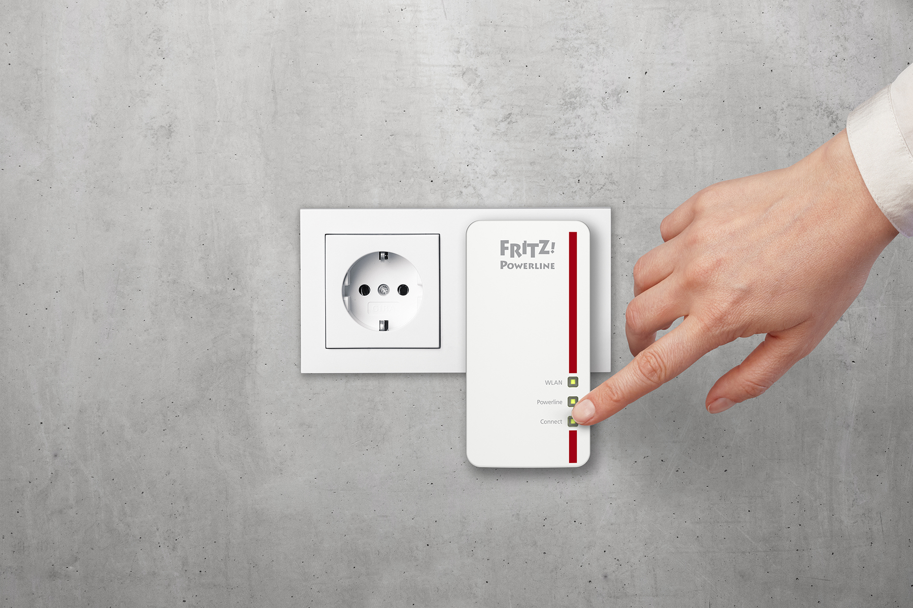 Dłoń dotykająca adaptera powerline wpiętego do gniazdka na szarej ścianie.