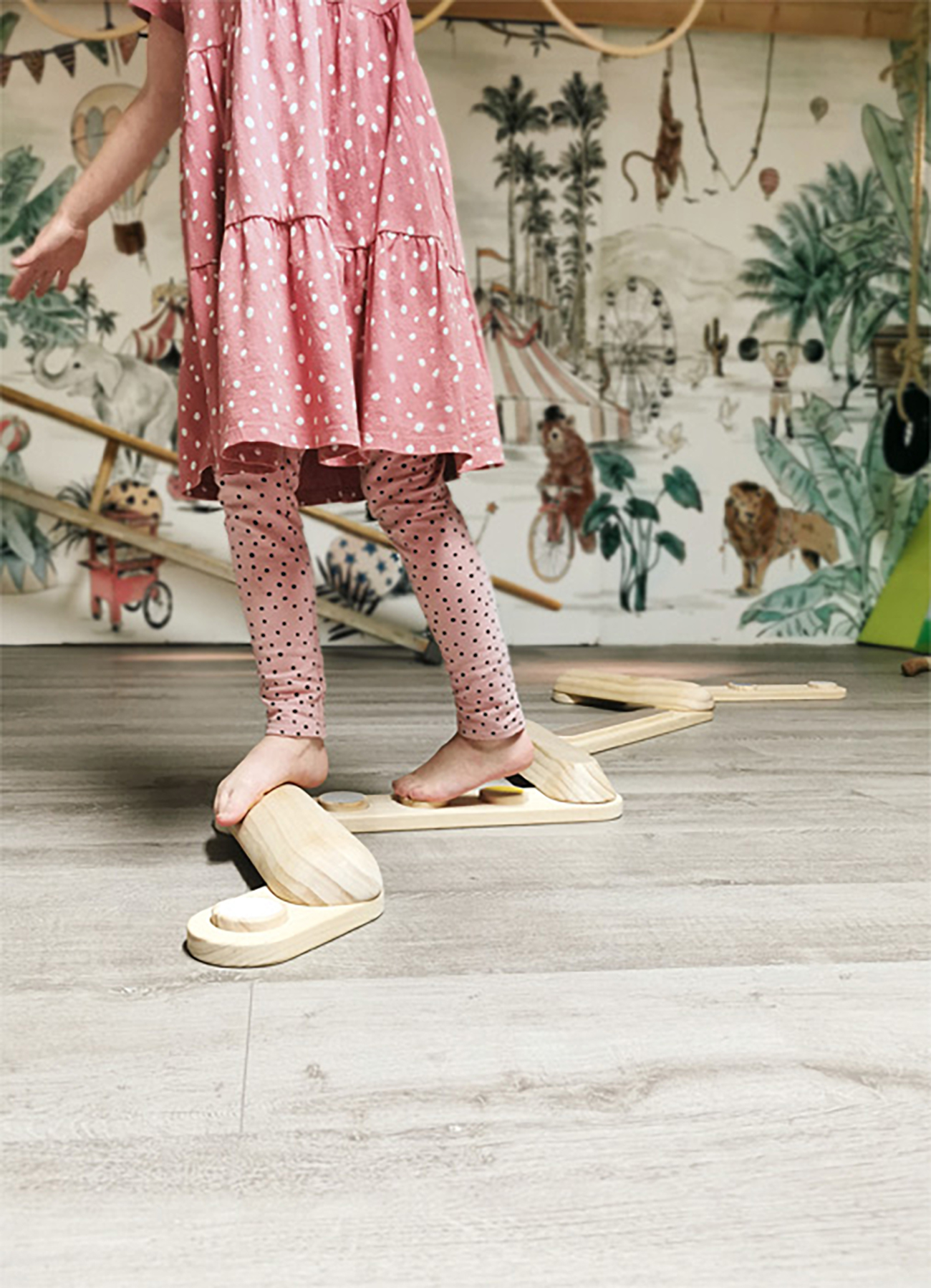 Bambino che cammina su travi di equilibrio in legno. Vestito rosa, leggings a pois. Murale della giungla.