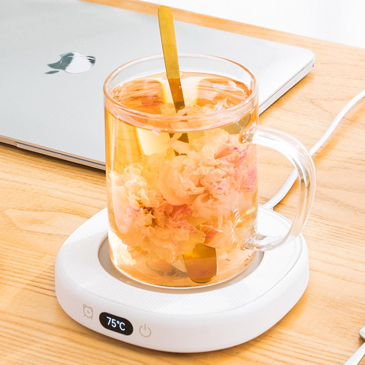 Ein Glasbecher mit Tee, auf einem weißen Tassenwärmer, mit einem Laptop im Hintergrund.