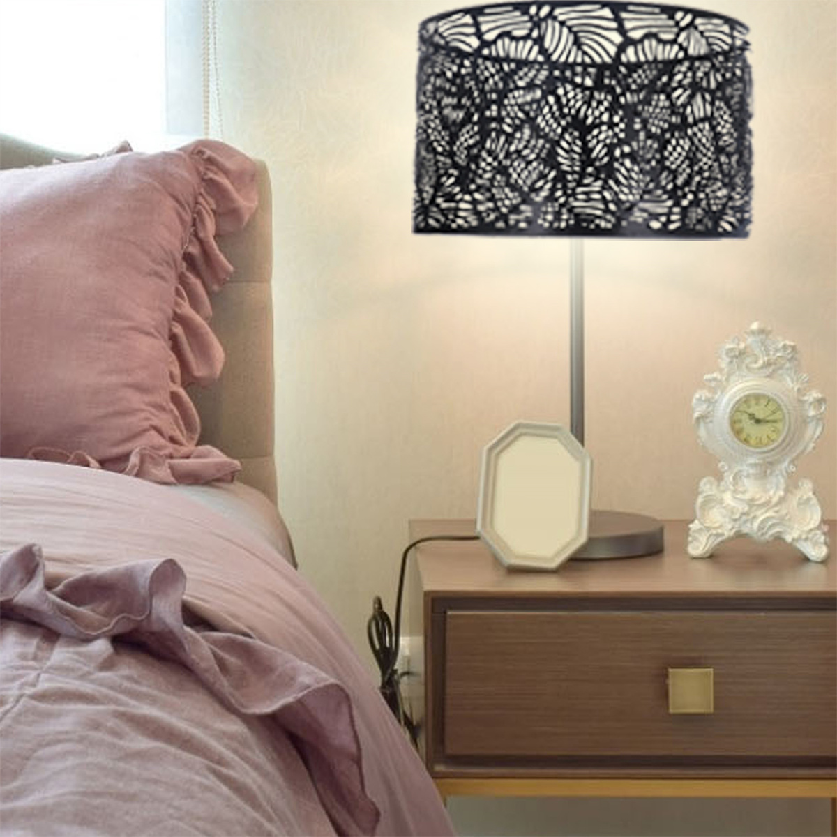 Eine Tischlampe mit schwarzem, gemustertem Schirm. Ein Schlafzimmer mit Bett, Nachttisch und Dekorationsartikeln.
