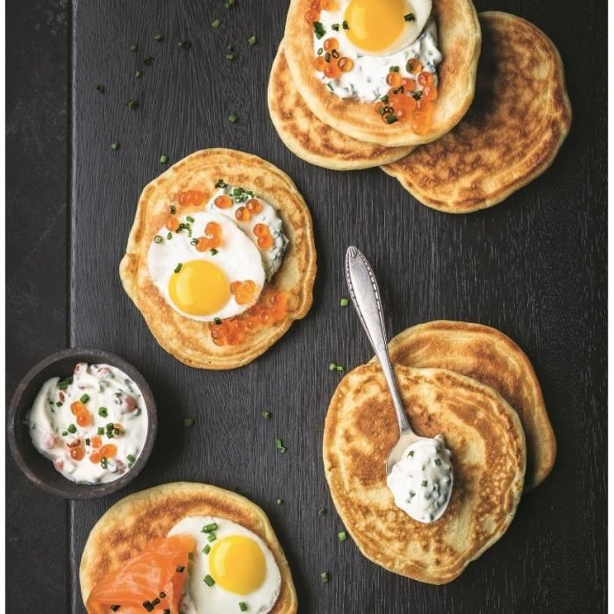 Panqueques con huevos, caviar y salmón. Hay un pequeño cuenco de salsa y una cuchara a un lado.
