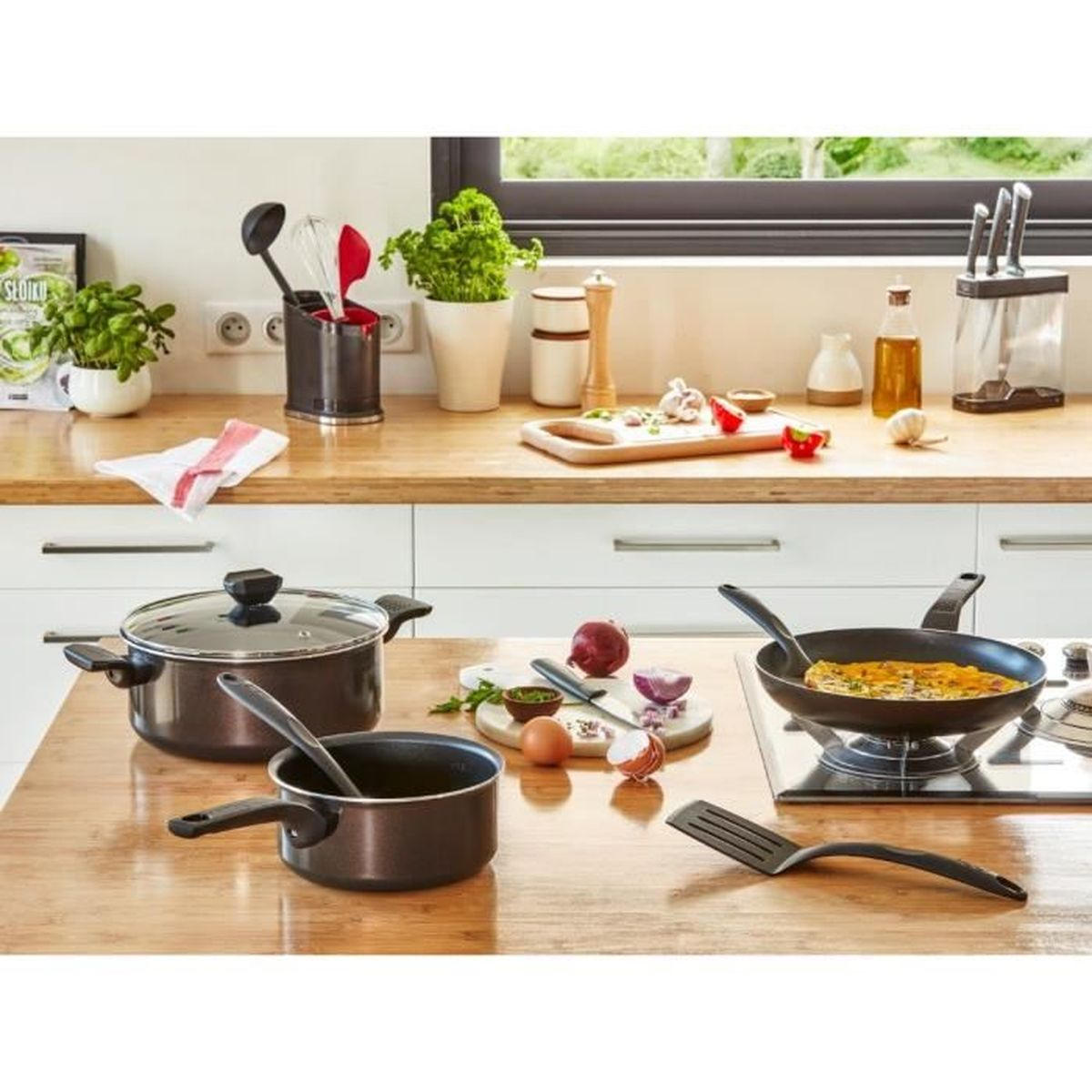 Escena de cocina con ollas, sartenes, utensilios e ingredientes.