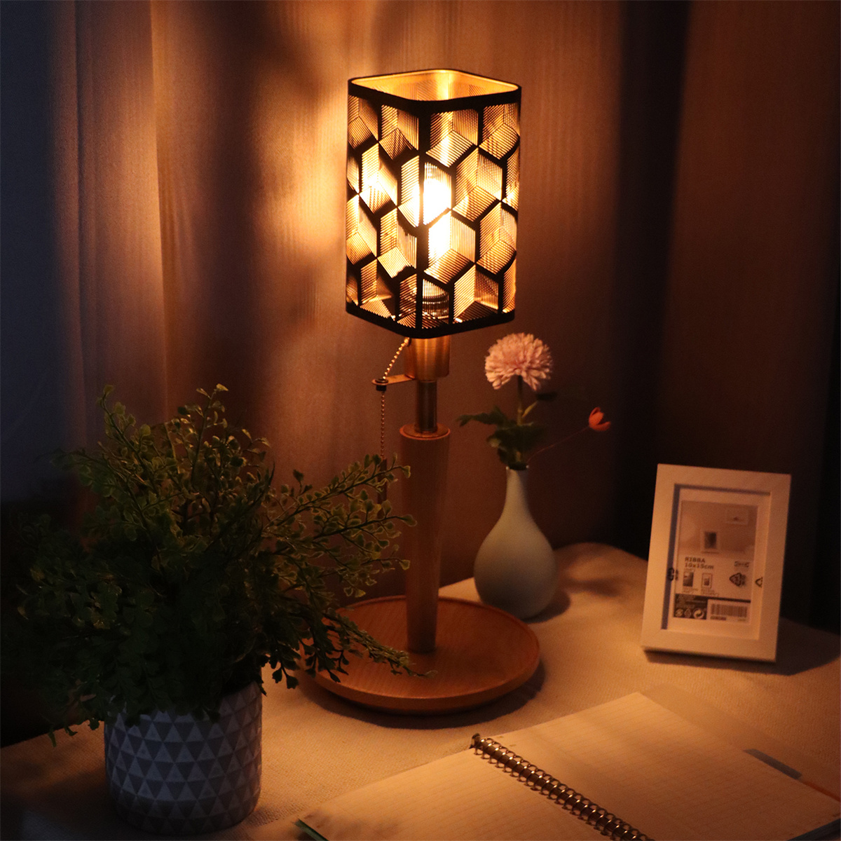 Beleuchtete Lampe auf einem Schreibtisch mit Blumen und Notizbuch. Warme Beleuchtung.