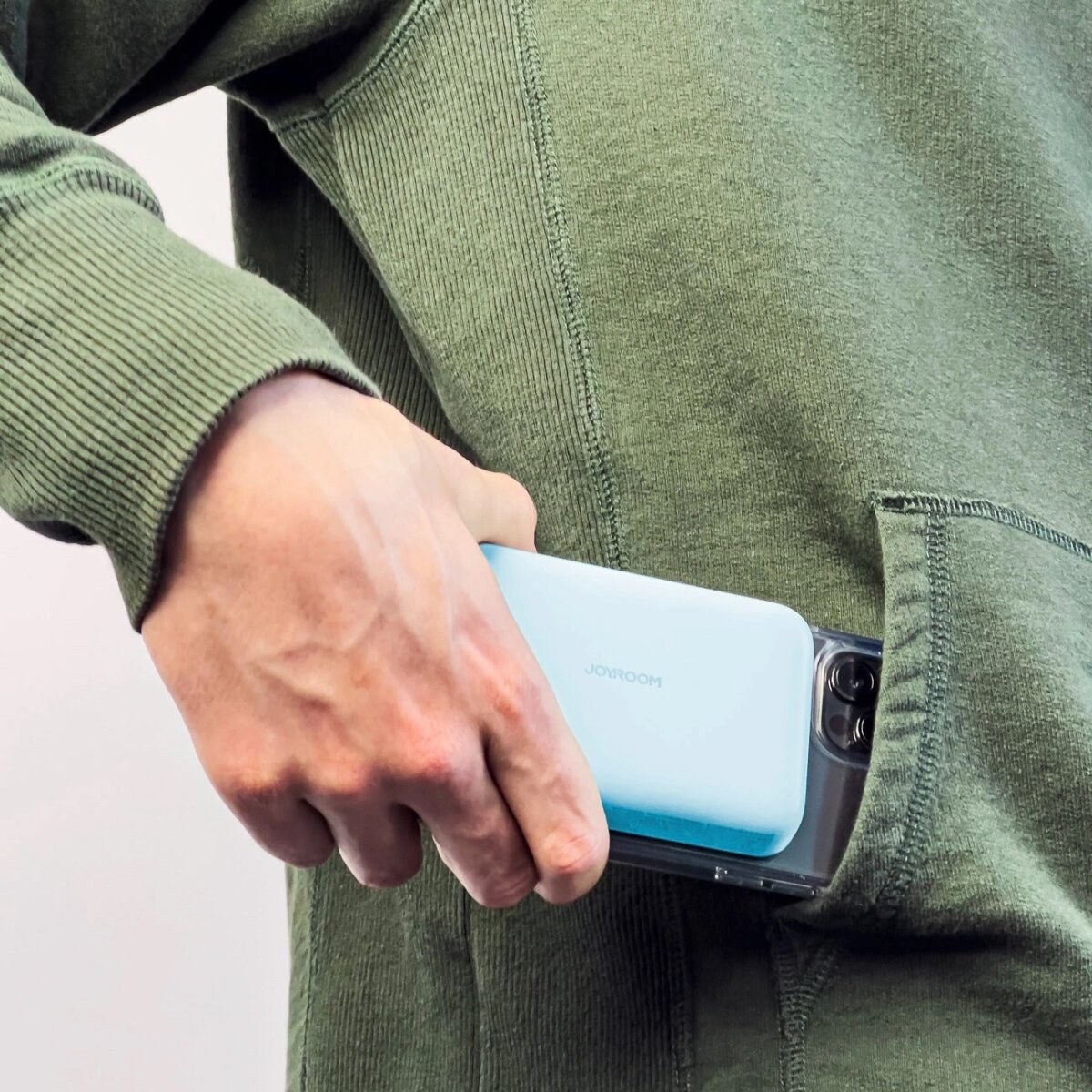Die Hand einer Person legt ein hellblaues Telefon in eine Kapuzentasche.