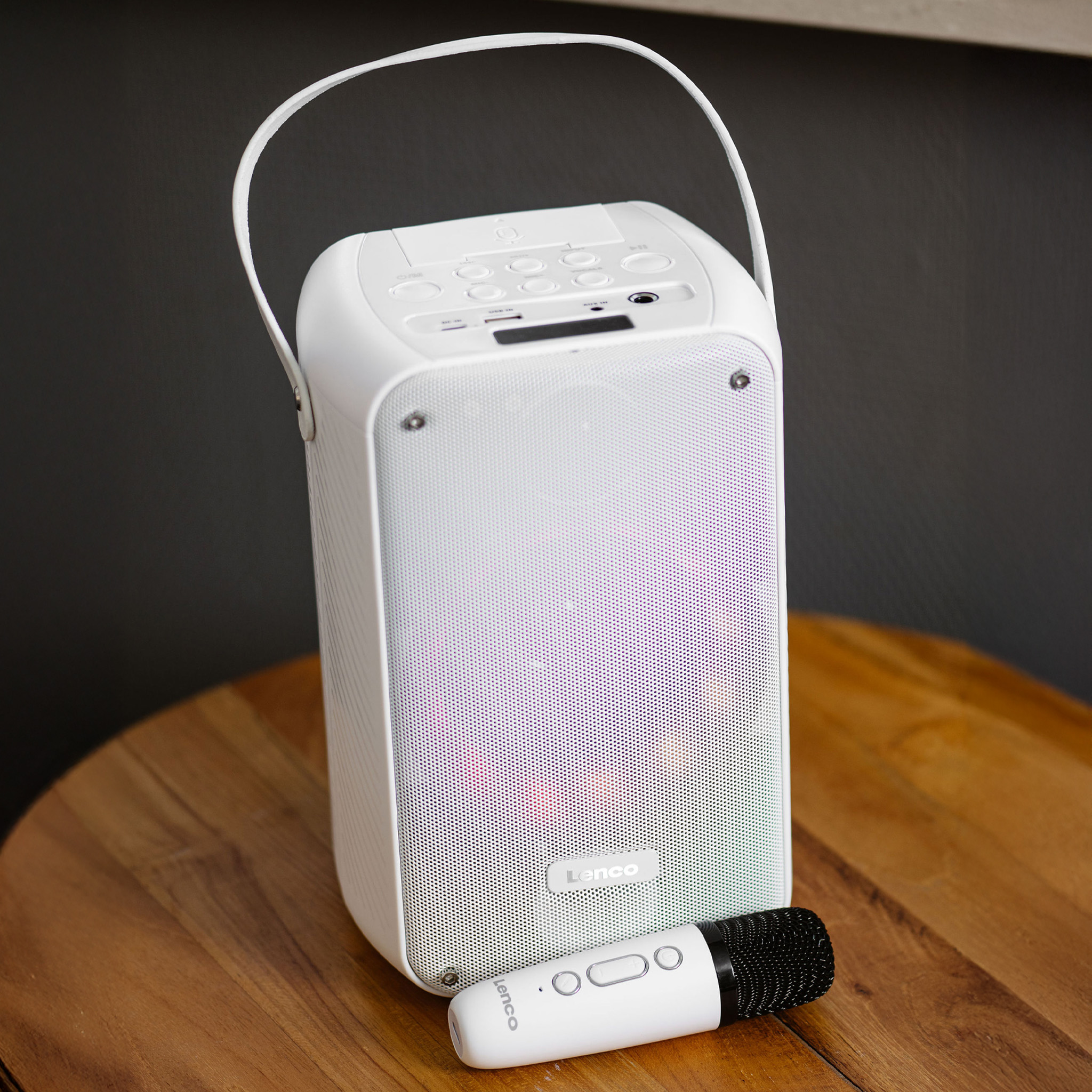 Witte speaker met handvat, microfoon en houten tafel als achtergrond.