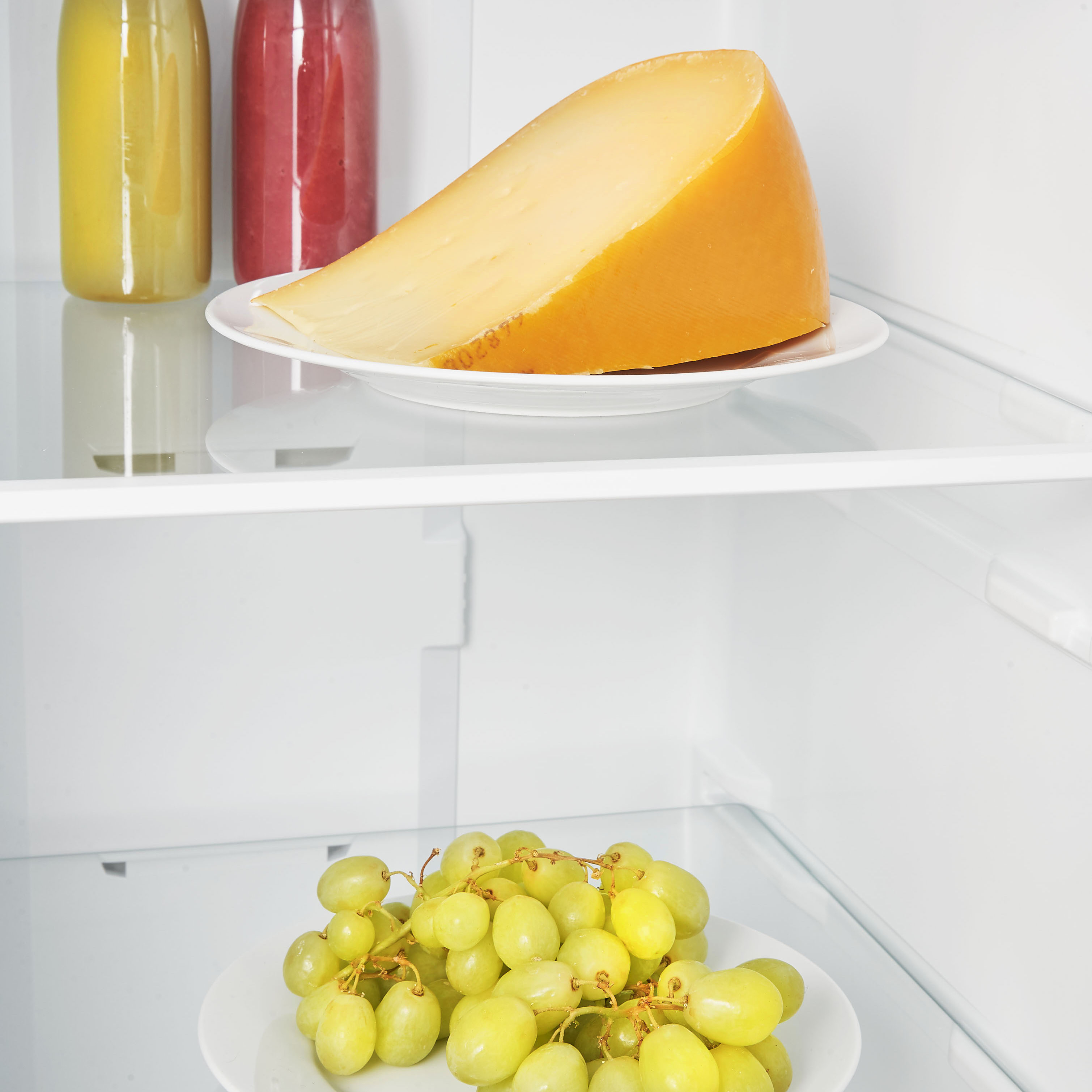 Cheese wedge on a white plate, with grapes below, in a refrigerator.