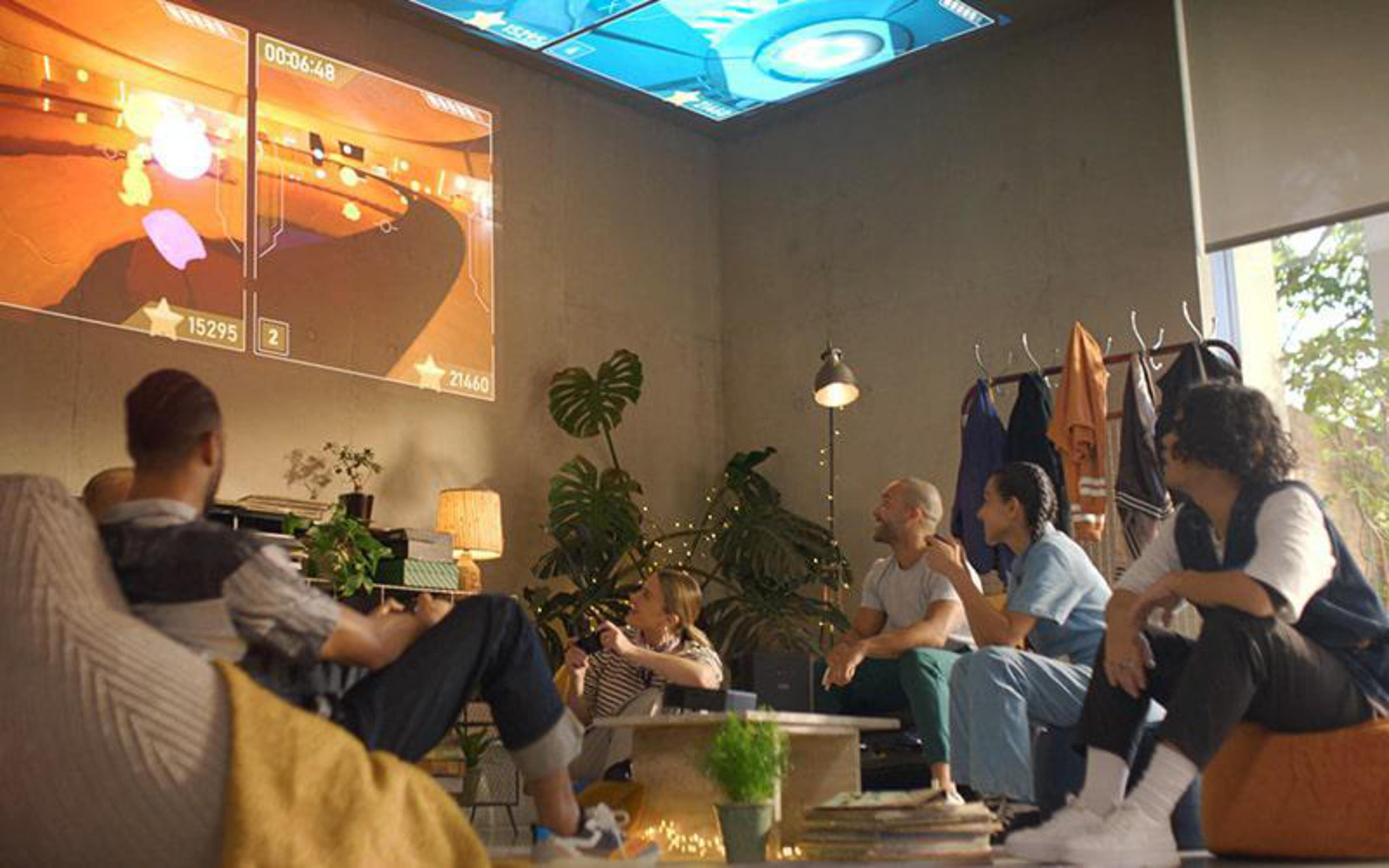Gruppe von Leuten, die in einem Raum Videospiele spielen. Spiele werden auf eine Leinwand an der Decke projiziert.