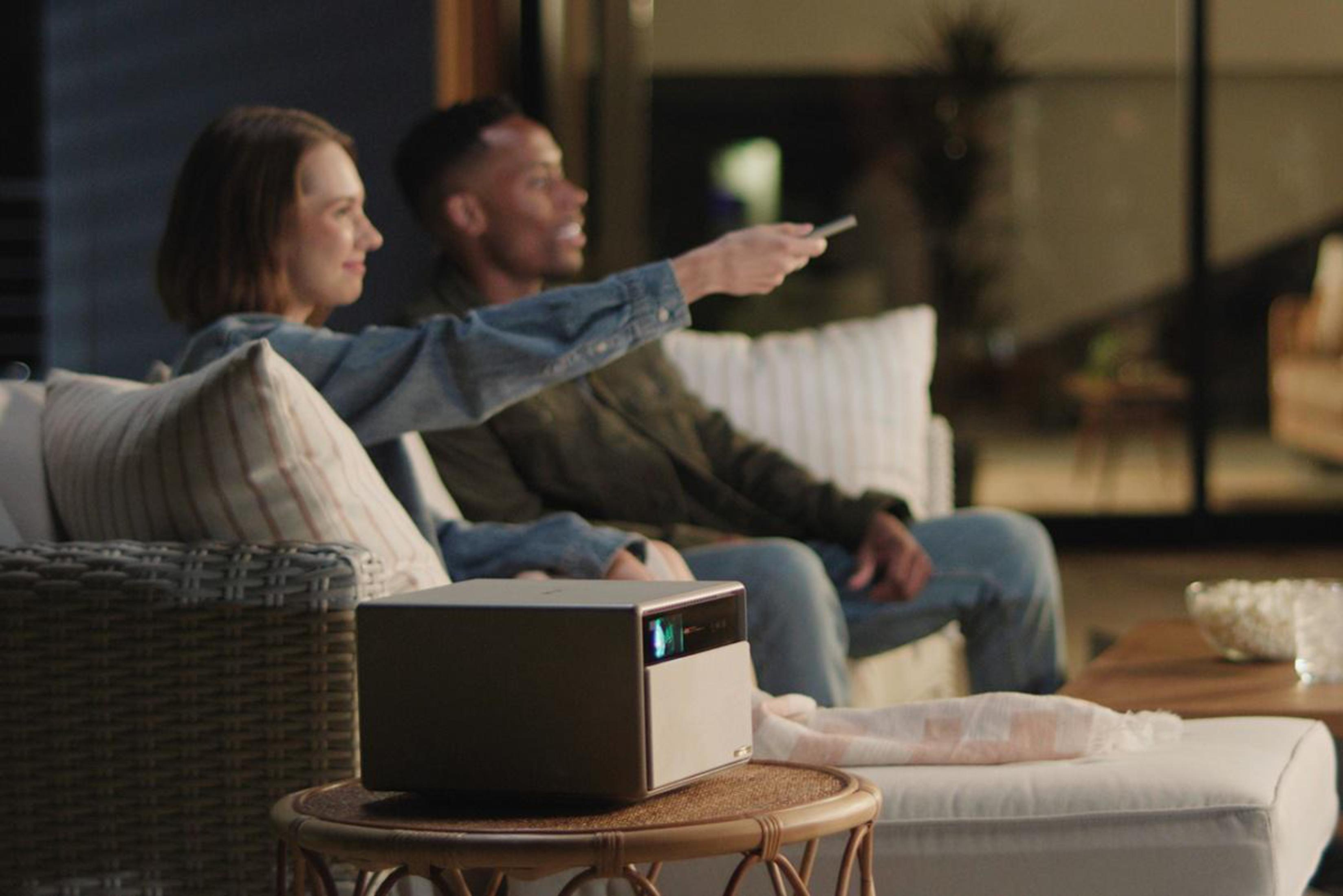 Para siedząca na kanapie ogląda film na projektorze, na zewnątrz w nocy.