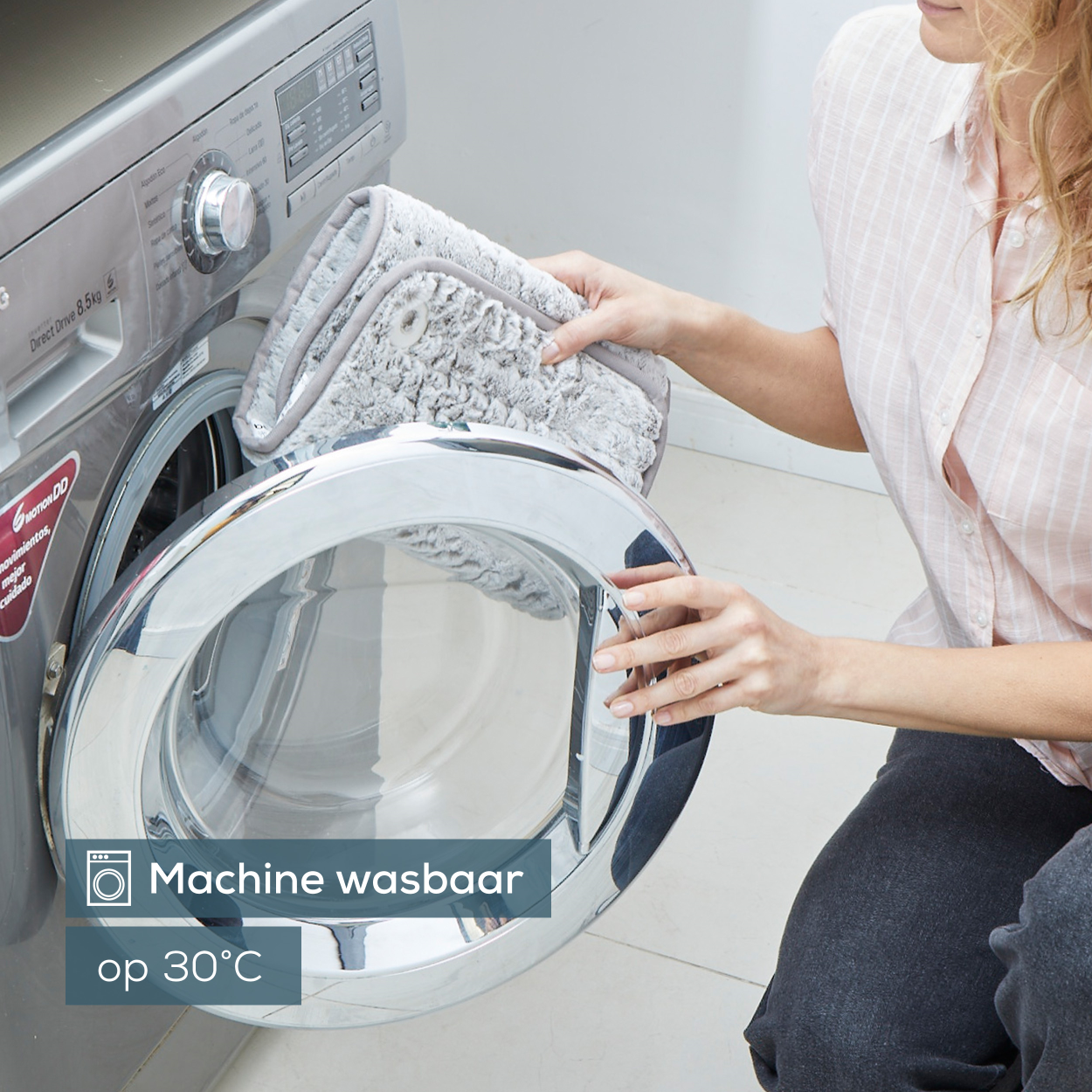 Vrouw stopt een grijze, bedrukte mat in een wasmachine. Tekst: Machinewasbaar op 30°C.
