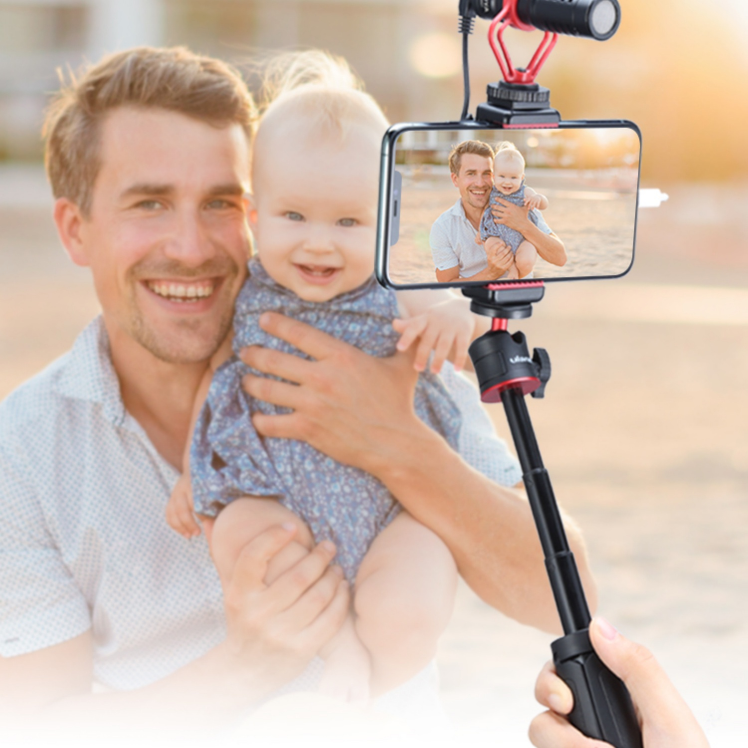 Ojciec trzymający dziecko i robiący selfie telefonem na patyku do selfie. Plaża, szczęśliwe miny.