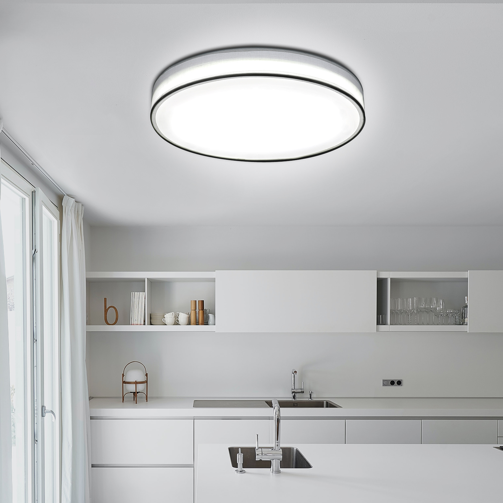 Biała kuchnia z dużą okrągłą lampą sufitową. Obecne są białe szafki, zlewozmywak i blat.