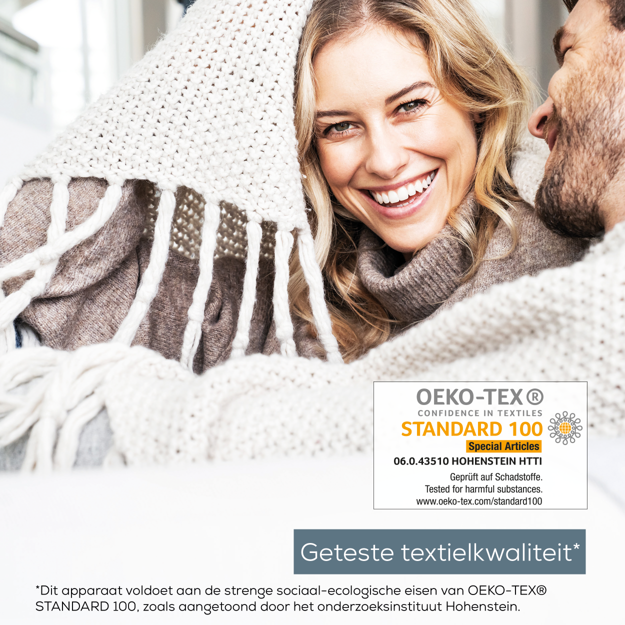 Coppia avvolta in una coperta, sorridente, con etichetta Oeko-Tex Standard 100.