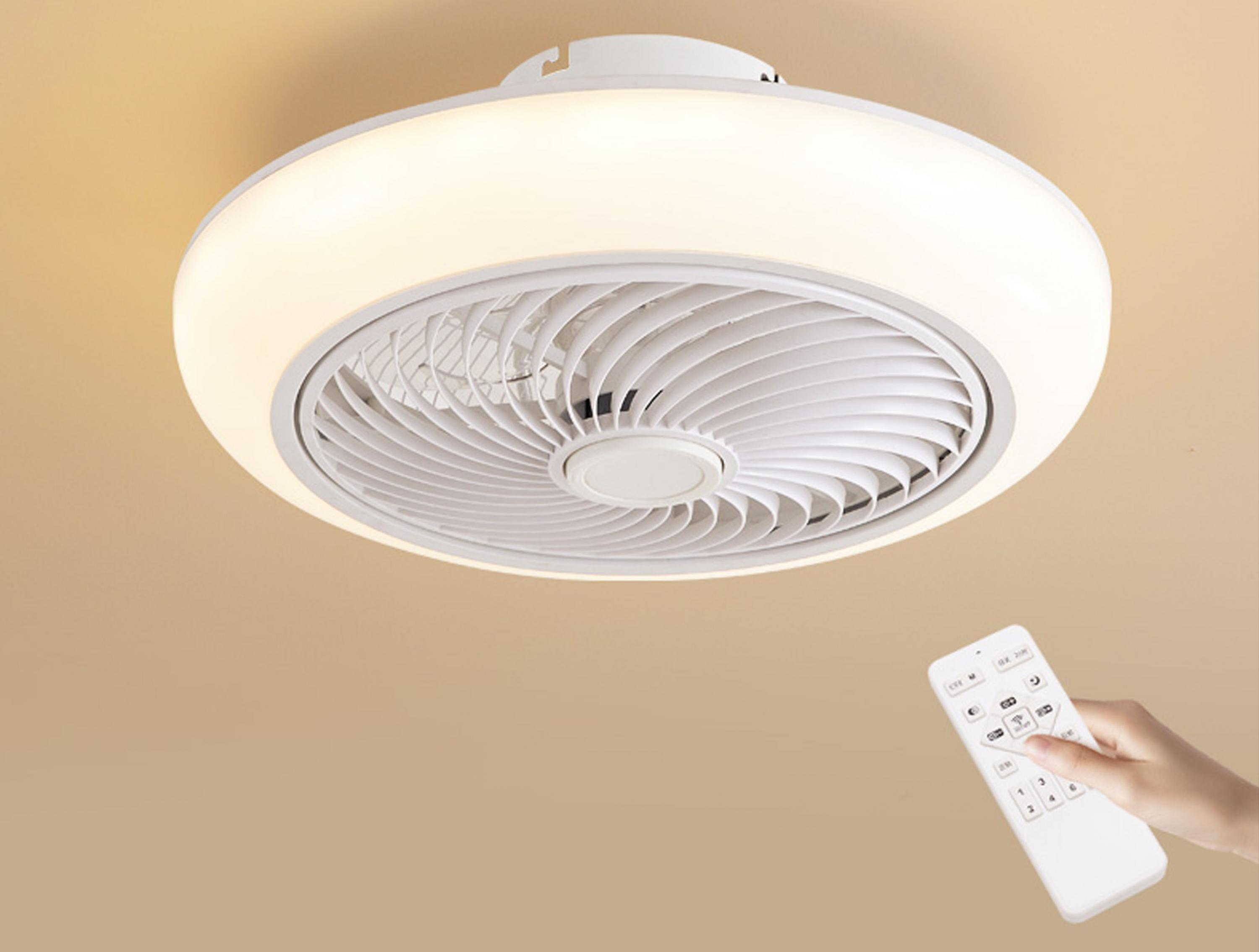 Un ventilador de techo con luz. Una mano usa un mando a distancia para operar el ventilador. El ventilador es blanco.