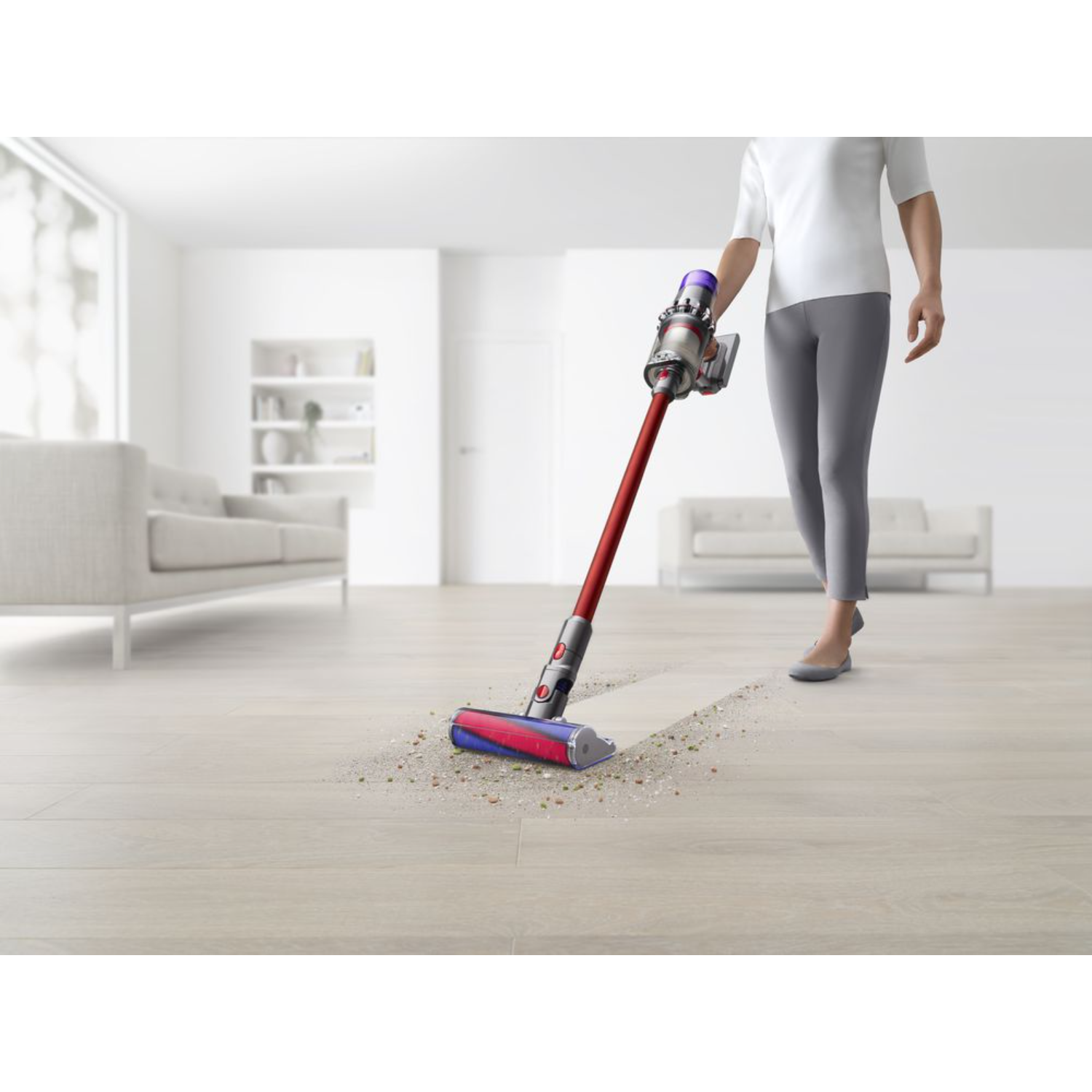 Osoba odkurza drewnianą podłogę czerwonym i srebrnym odkurzaczem Dyson.
