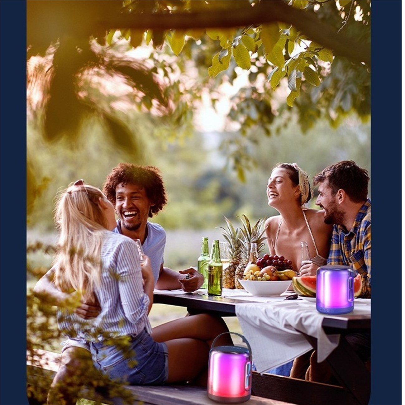 Freundesgruppe lacht, versammelt an einem Tisch mit Essen, Getränken und einem tragbaren Lautsprecher.