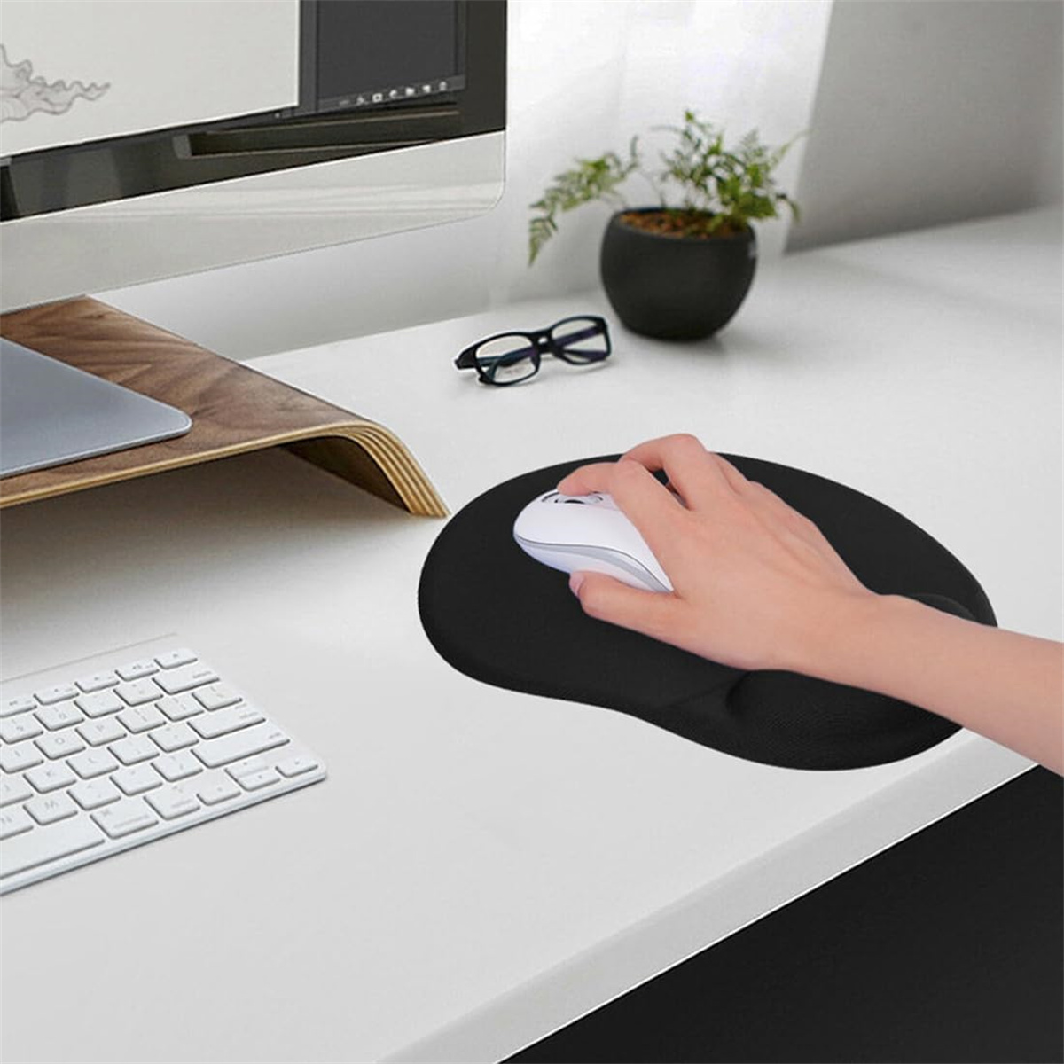 Hand benutzt eine weiße Maus auf einem schwarzen Mauspad. Tastatur und Brille sind ebenfalls sichtbar.