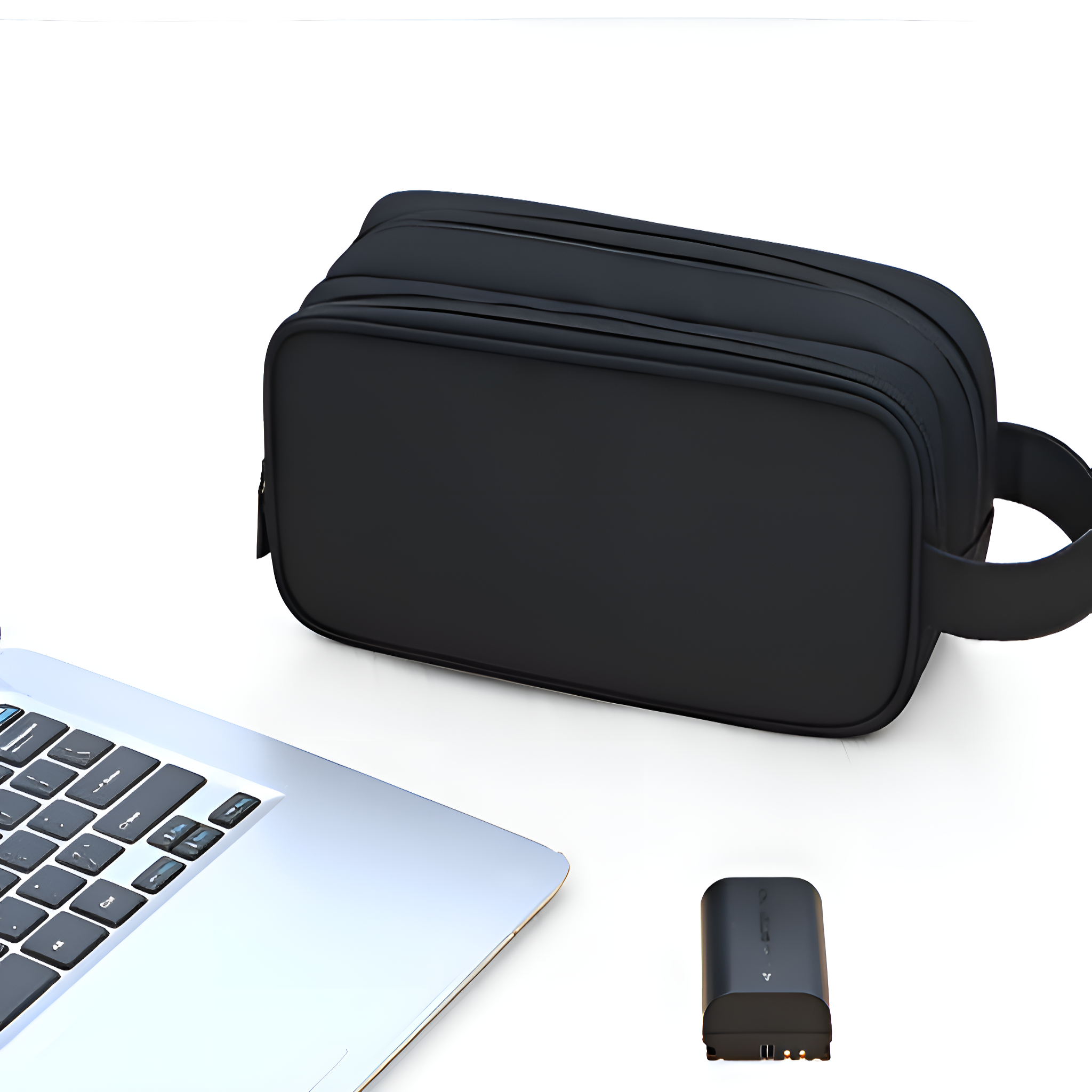 Schwarze Kulturtasche, ein Laptop und ein kleines Batterieladegerät auf weißem Untergrund.