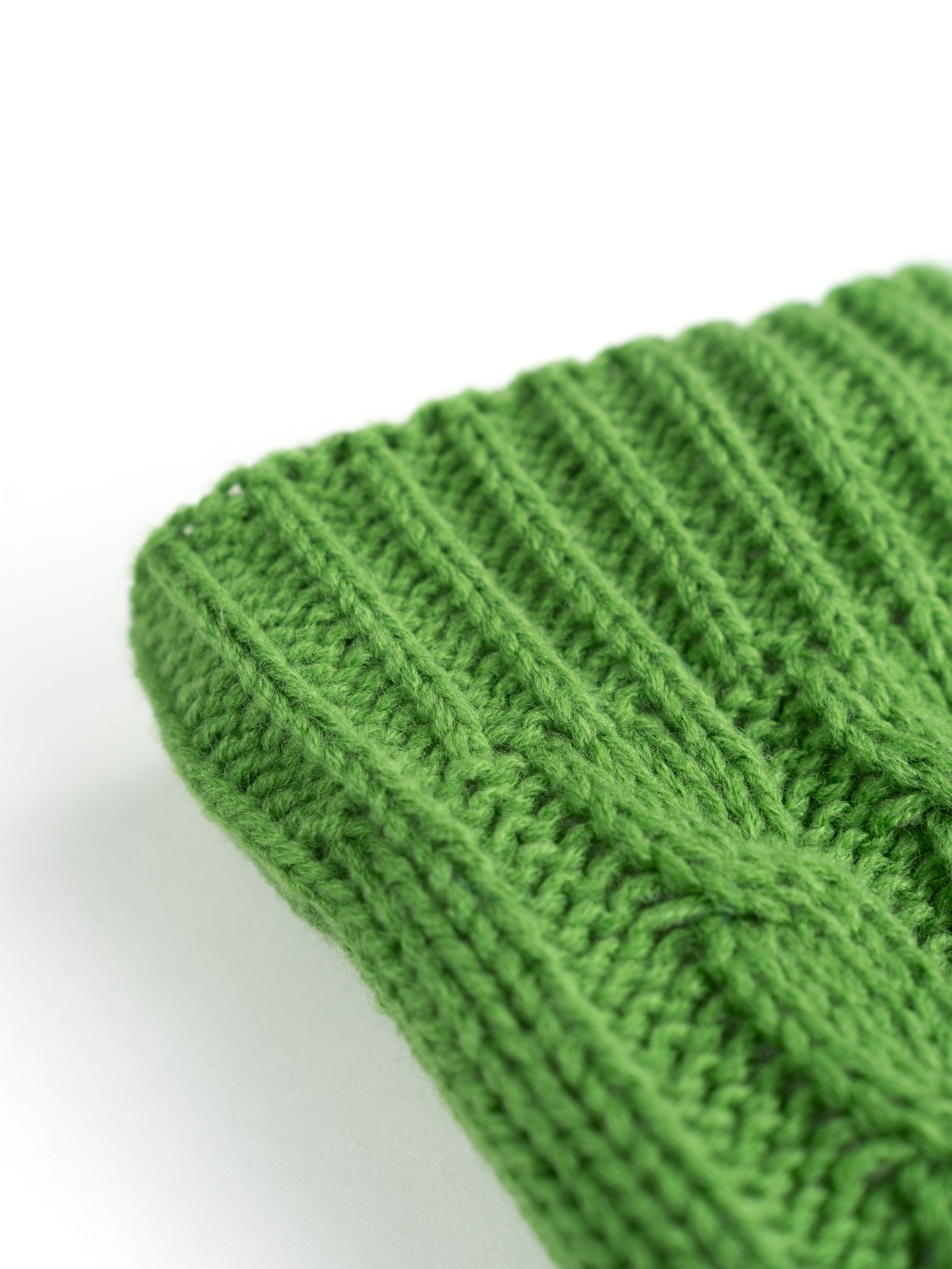 Nahaufnahme einer grünen Strickmütze. Die Mütze ist aus einem Rippenmuster gefertigt.
