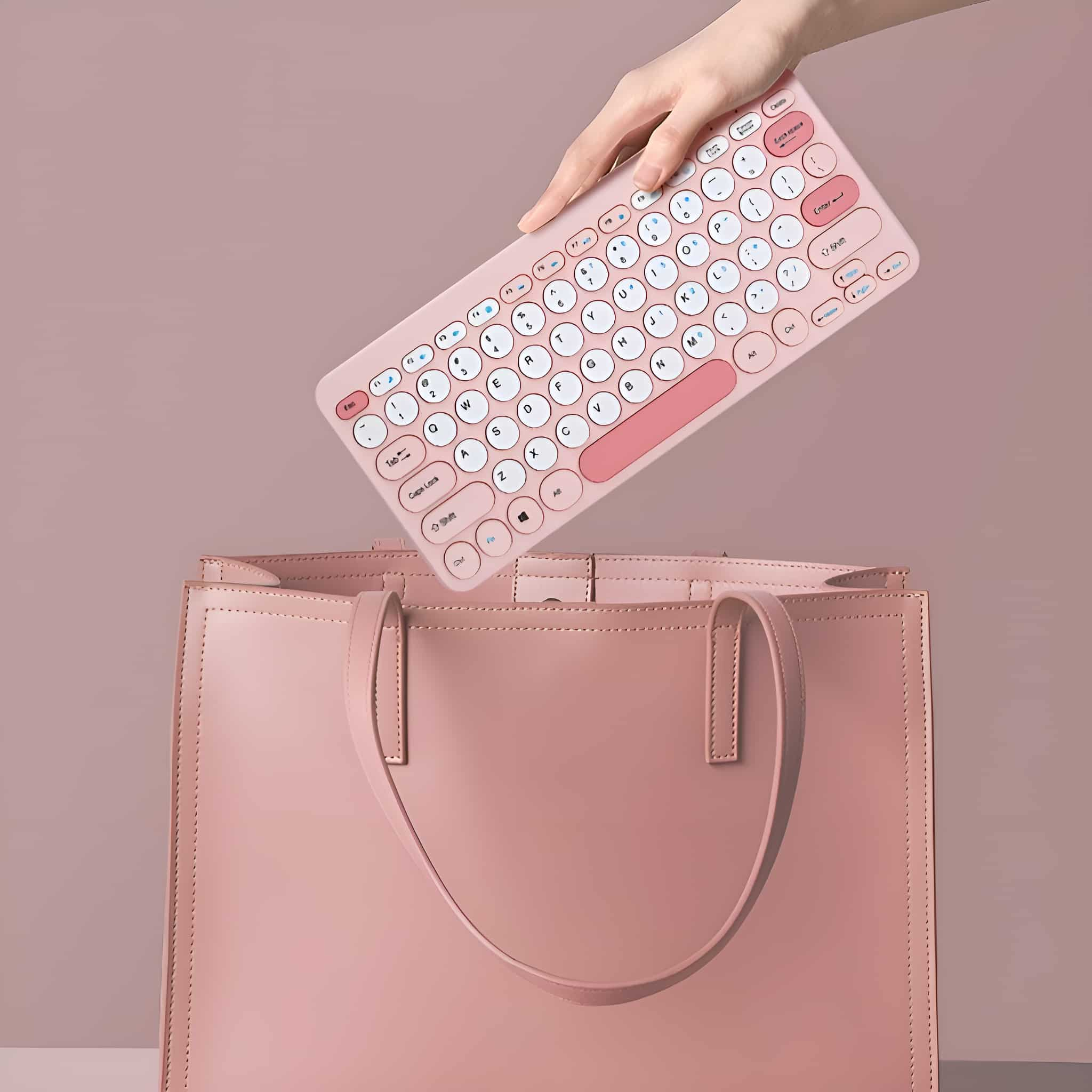 Eine Hand, die eine pinkfarbene Tastatur über einer pinkfarbenen Handtasche hält. Die Tastatur ist weiß und pink mit runden Tasten.