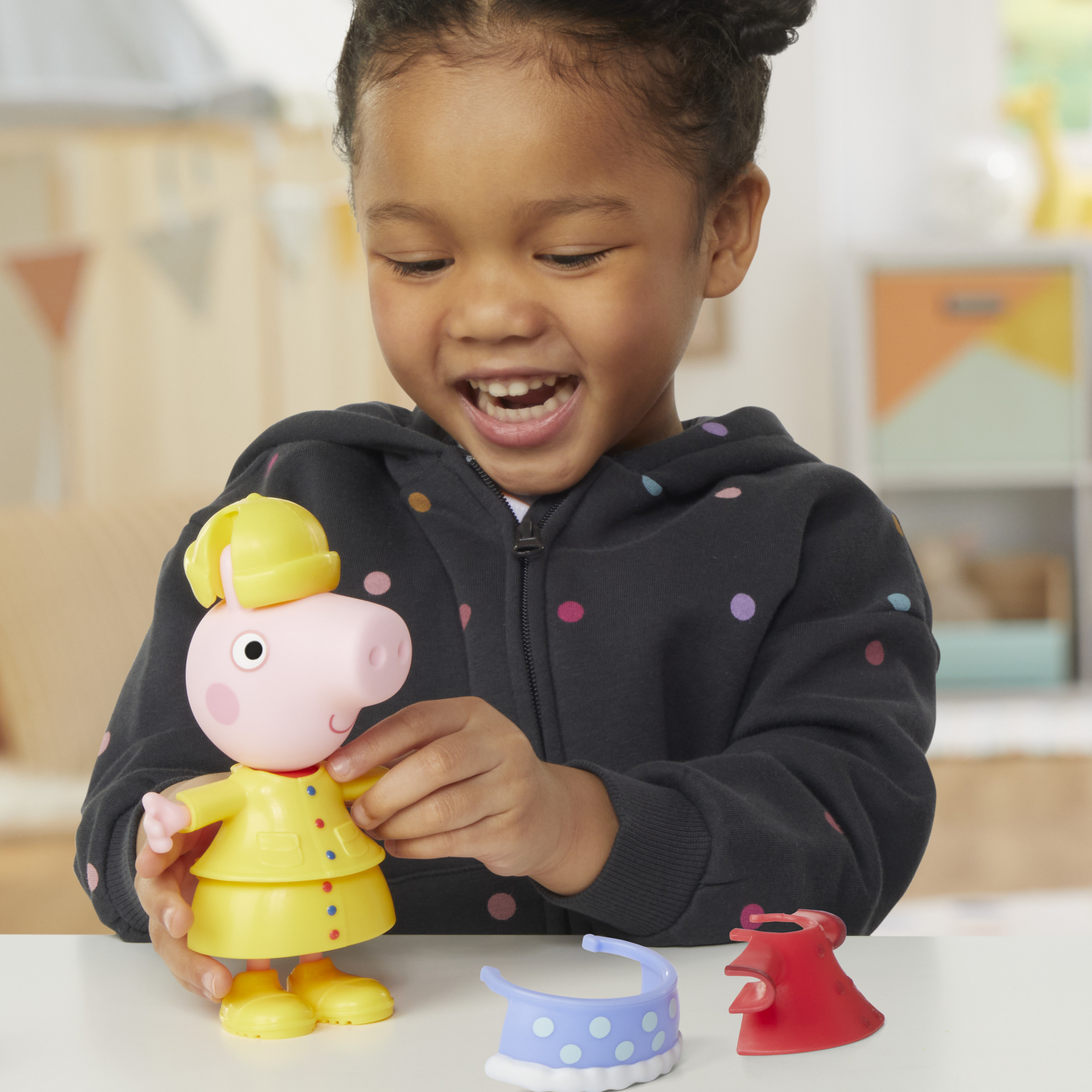 Una niña jugando con un juguete de Peppa Pig. Ella está sosteniendo la muñeca y ropa para vestir.