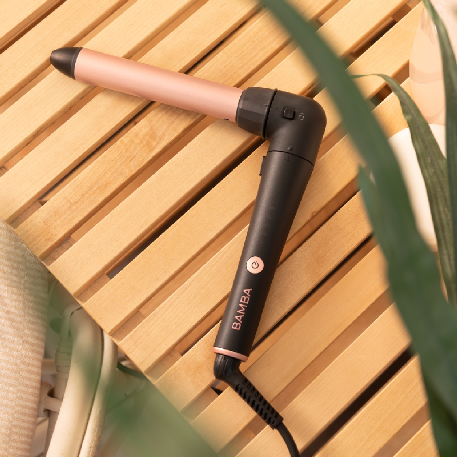 Arricciacapelli nero e oro rosa su legno, foglie verdi.
