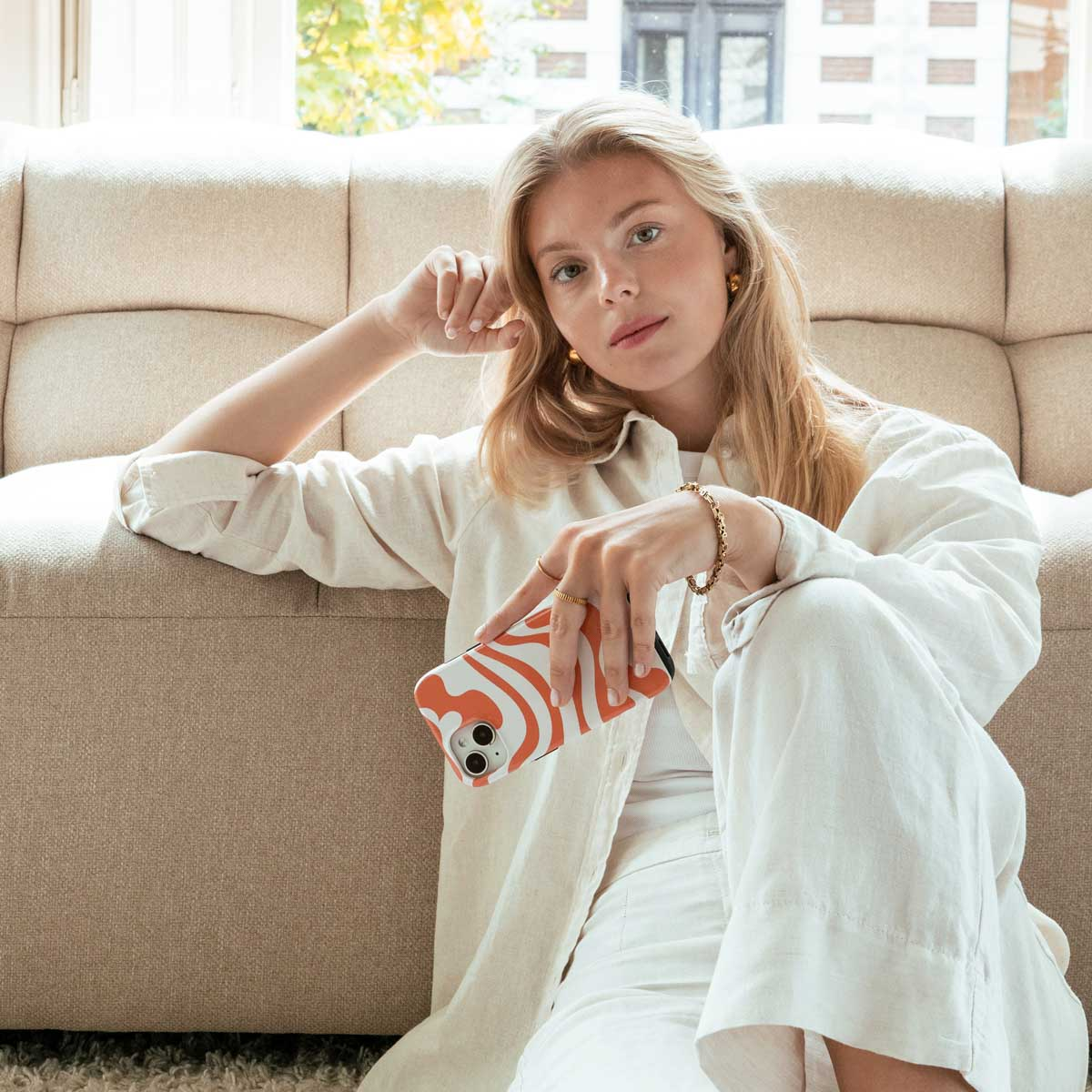 Femme en vêtements de lin tenant un téléphone avec un motif orange et blanc.