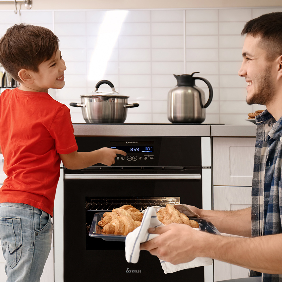 Ein Vater und Sohn backen. Der Sohn zeigt auf den Ofen. Croissants auf einem Blech.