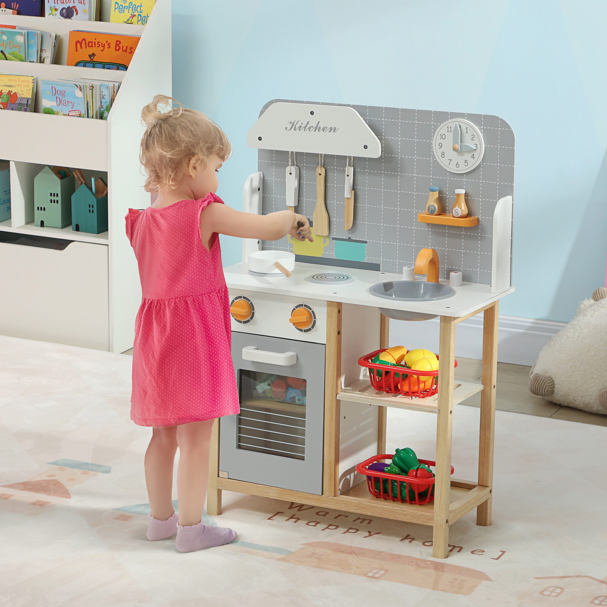 Una niña juega con una cocina de juguete de madera. La cocina tiene un fregadero, horno y estantes con juguetes.