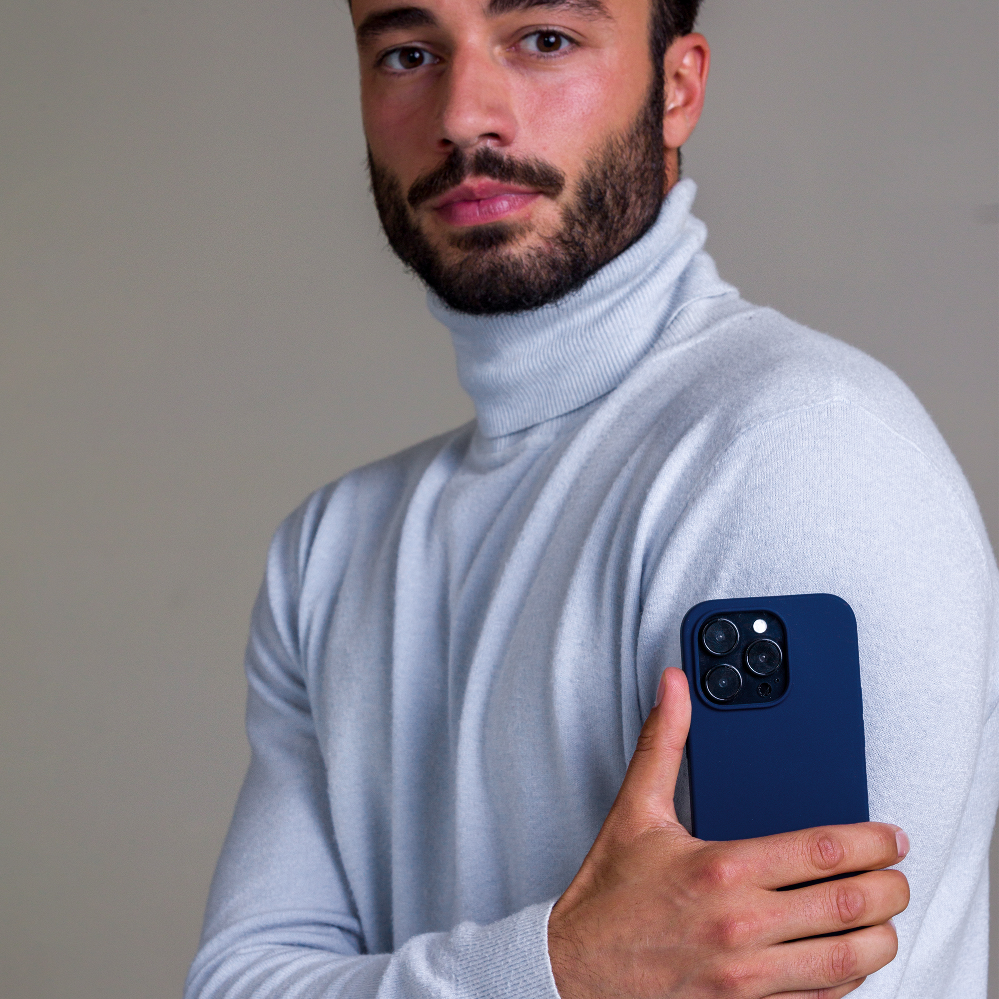 Un uomo tiene in mano un telefono blu navy con un dolcevita azzurro.