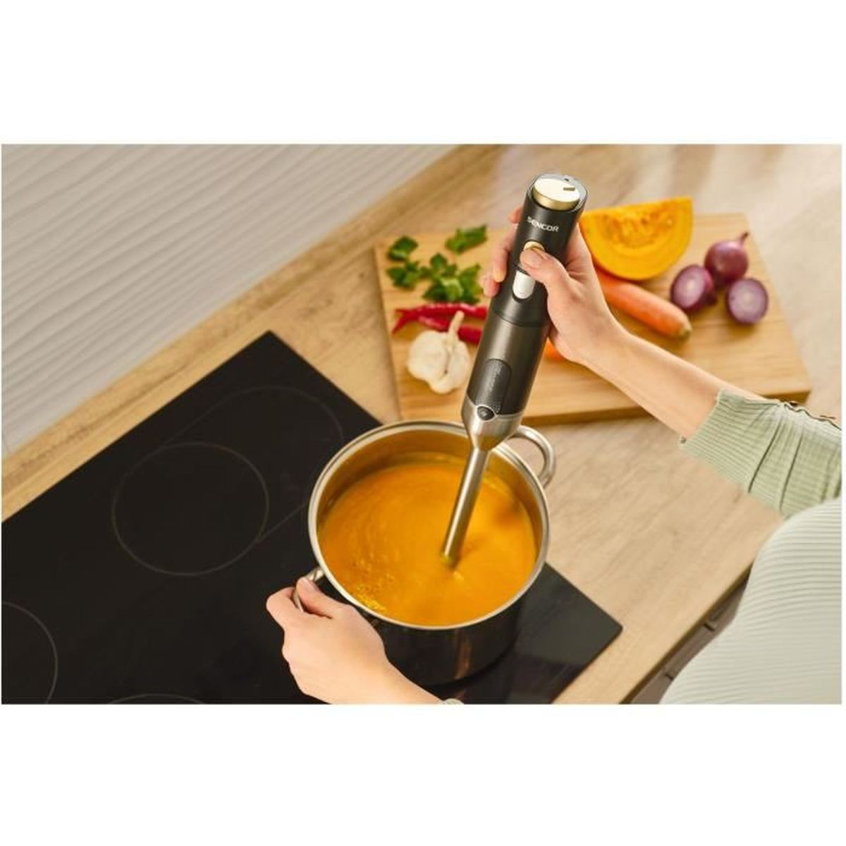Una persona che frulla una zuppa in una pentola con un frullatore a immersione su una superficie di legno.
