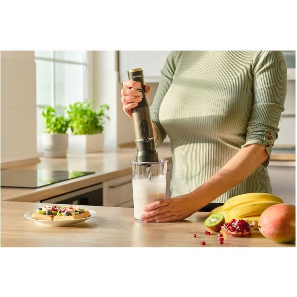 Una donna usa un frullatore a immersione per mescolare gli ingredienti in un bicchiere.