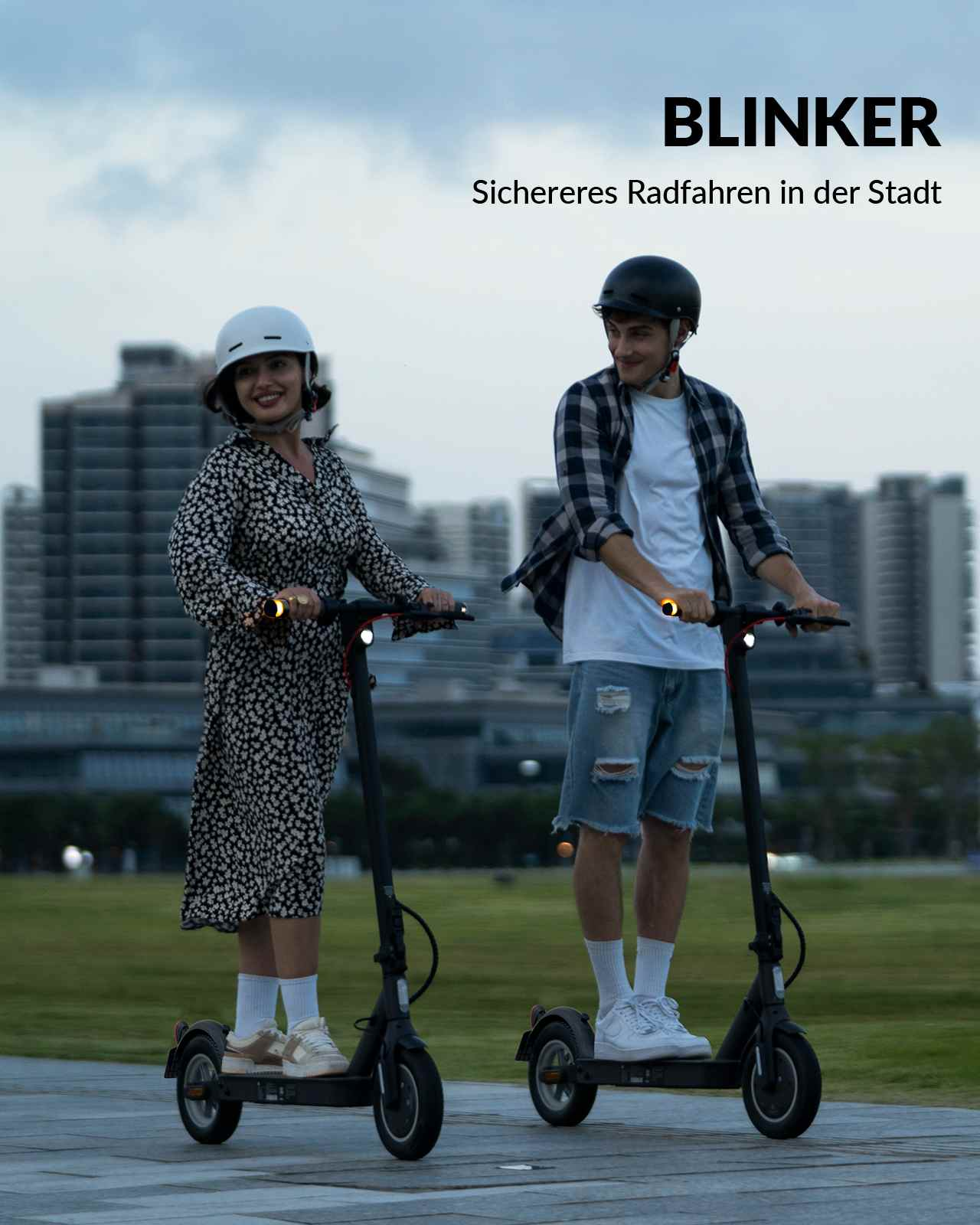 Zwei Personen auf Elektrorollern, tragen Helme, fahren auf einem Weg, mit Text 'BLINKER'.