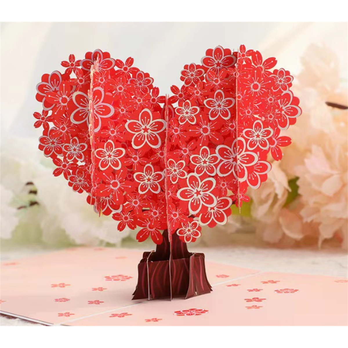 Rote, herzförmige Pop-up-Grußkarte mit weißen Blumenausschnitten auf rosa Fläche.