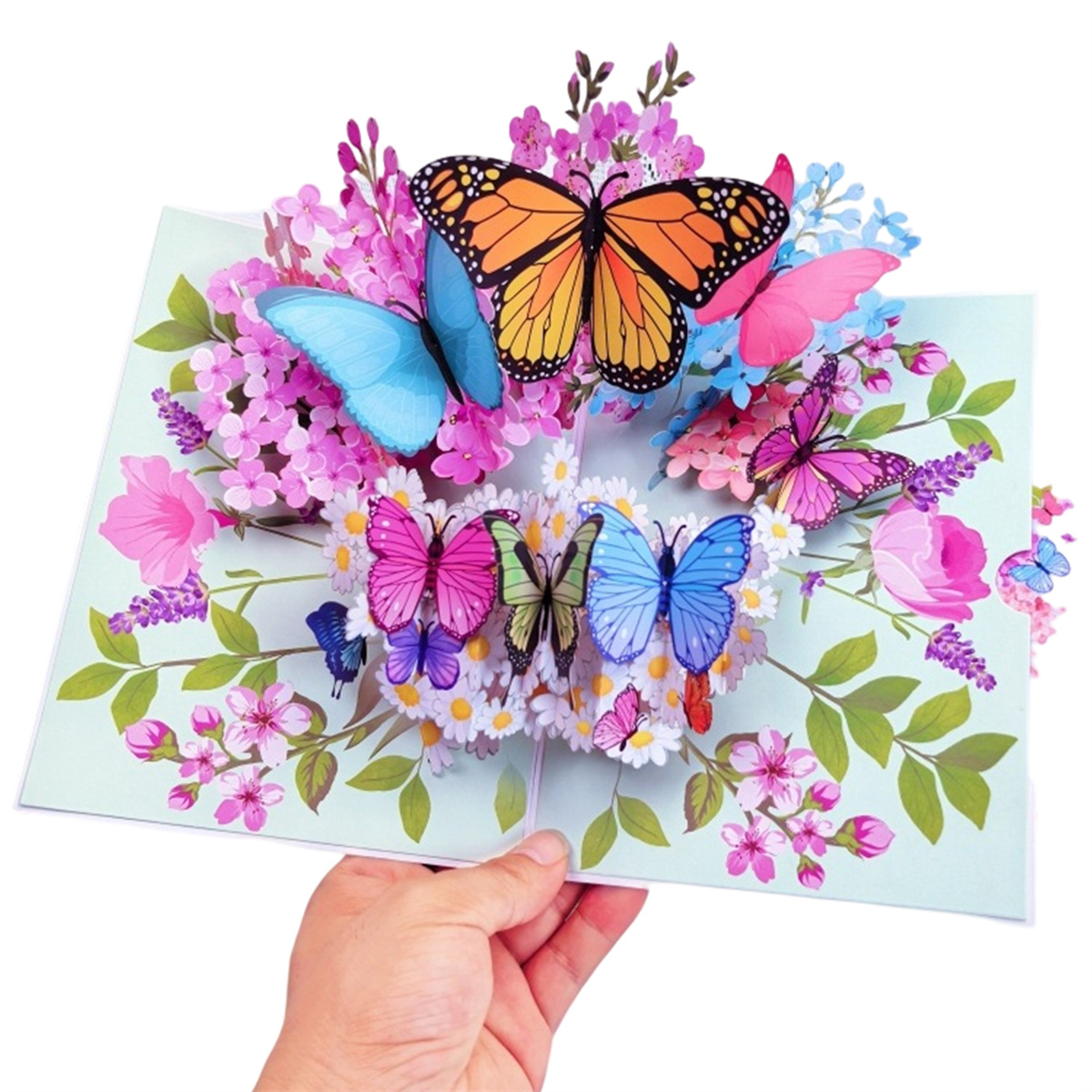 Eine Pop-up-Grußkarte mit Schmetterlingen und Blumen. Eine Hand hält die Karte offen.