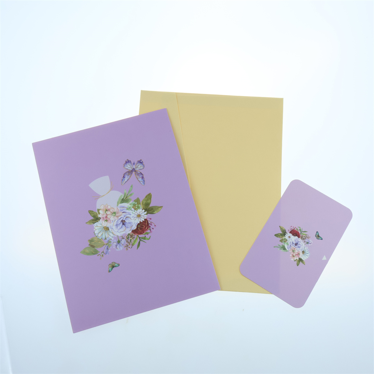 Drei Grußkarten mit Blumendesigns und Schmetterlingen. Lavendel, Gelb und Rosa. Weißer Hintergrund.