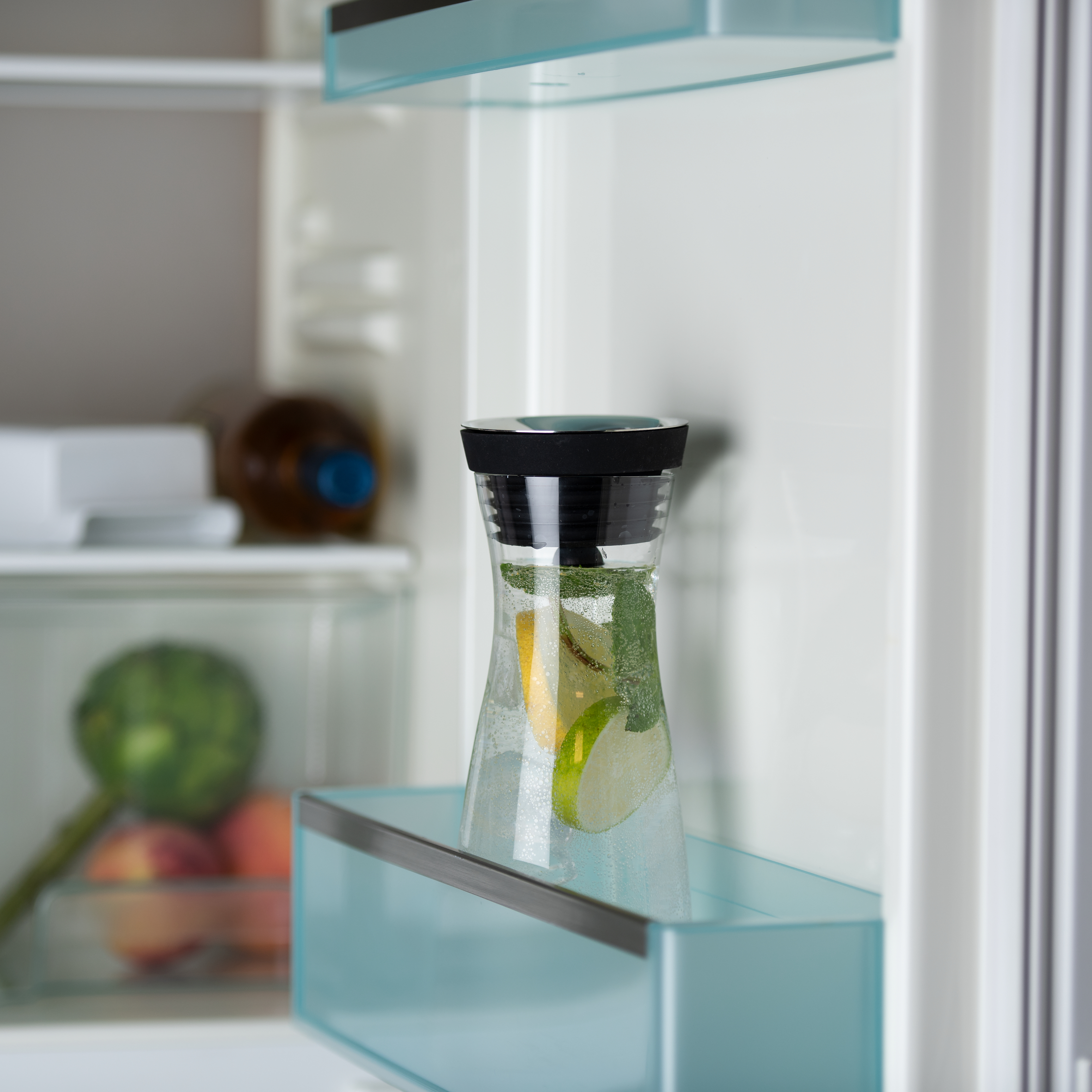 Kühlschrank-Innenraum. Eine Glaskanne mit Fruchtscheiben und Wasser steht auf einem Regal.