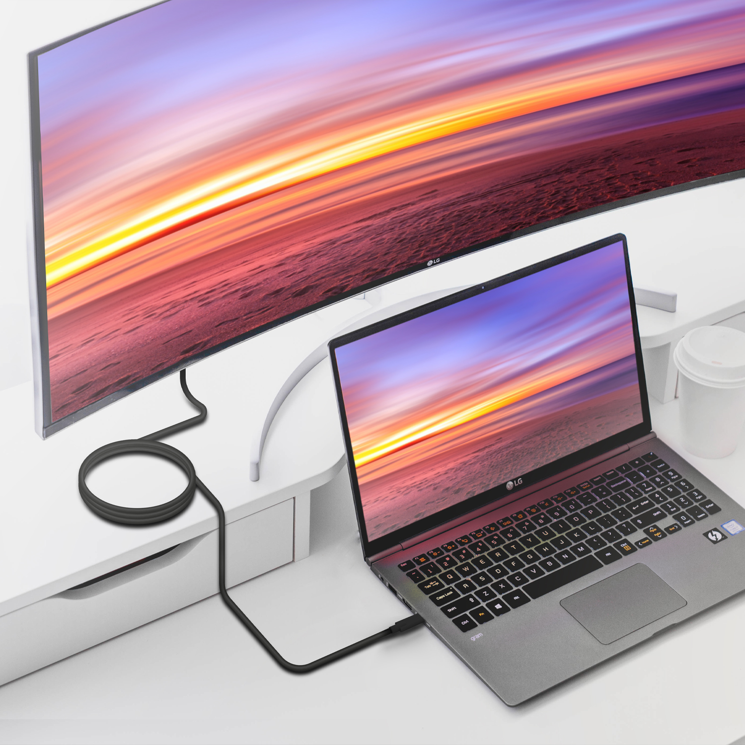 Een laptop aangesloten op een grote gebogen monitor. De monitor toont een zonsondergangscène. De laptop staat op een wit bureau.