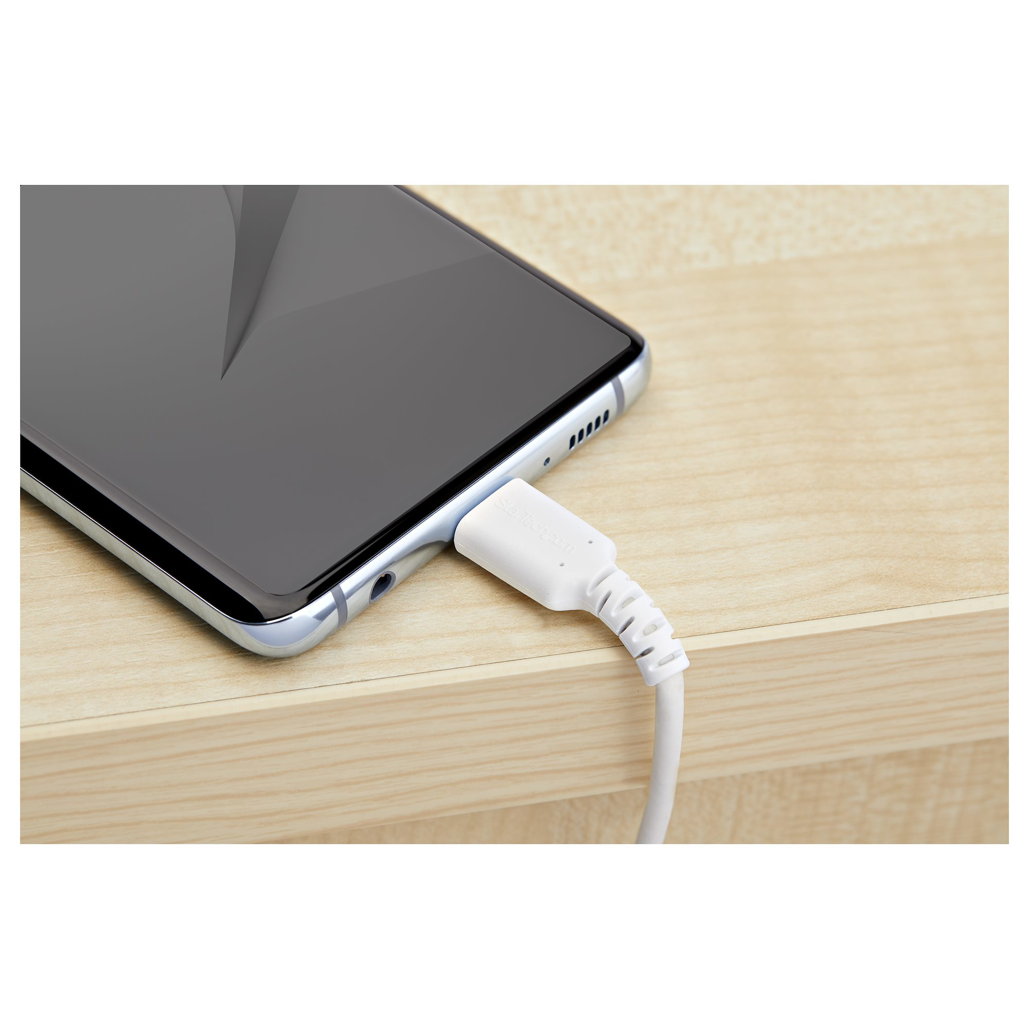 A white USB-C cable is connected to a black smartphone on a wooden surface.