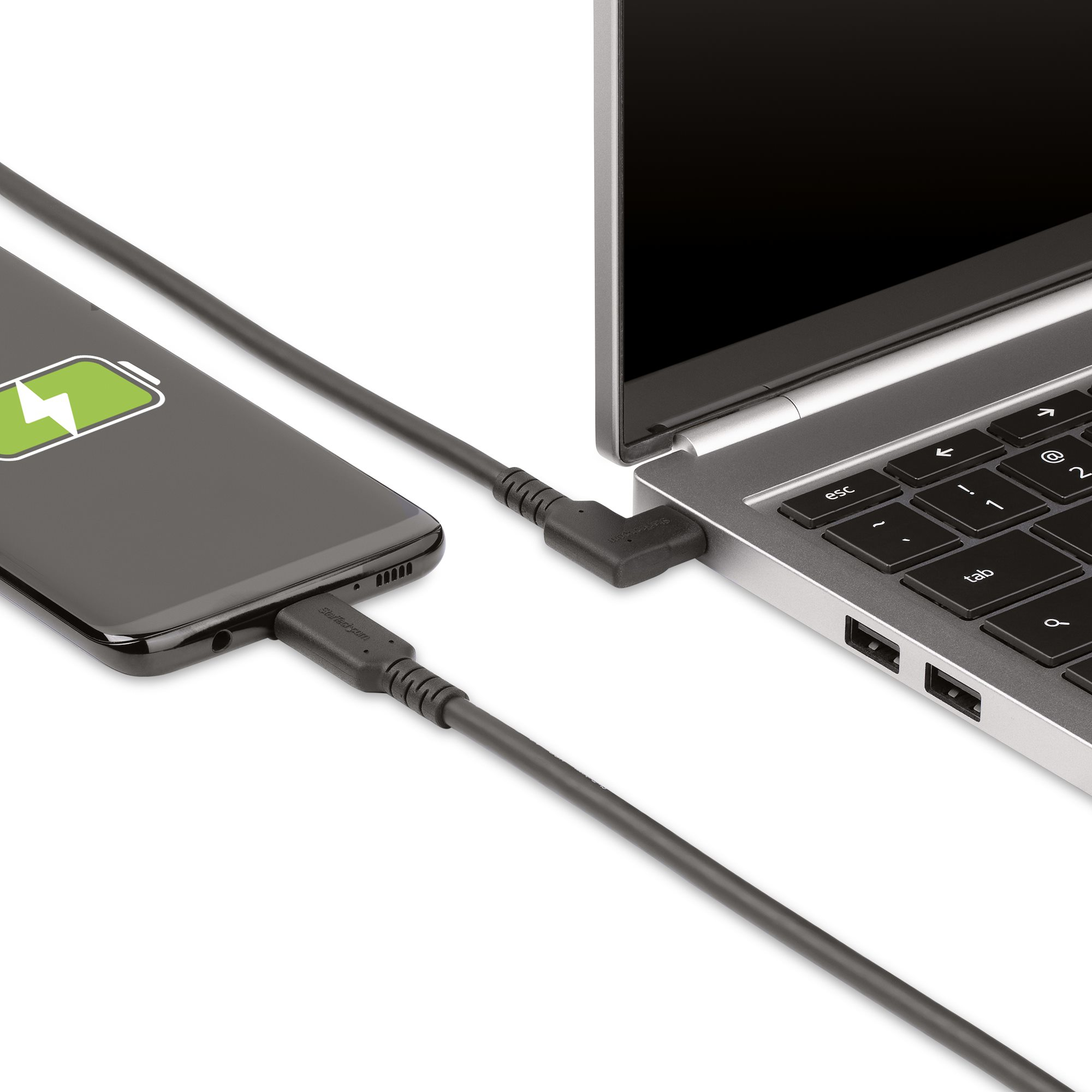 Ein schwarzes Telefon, das einen Laptop mit grauem Ladekabel auflädt.
