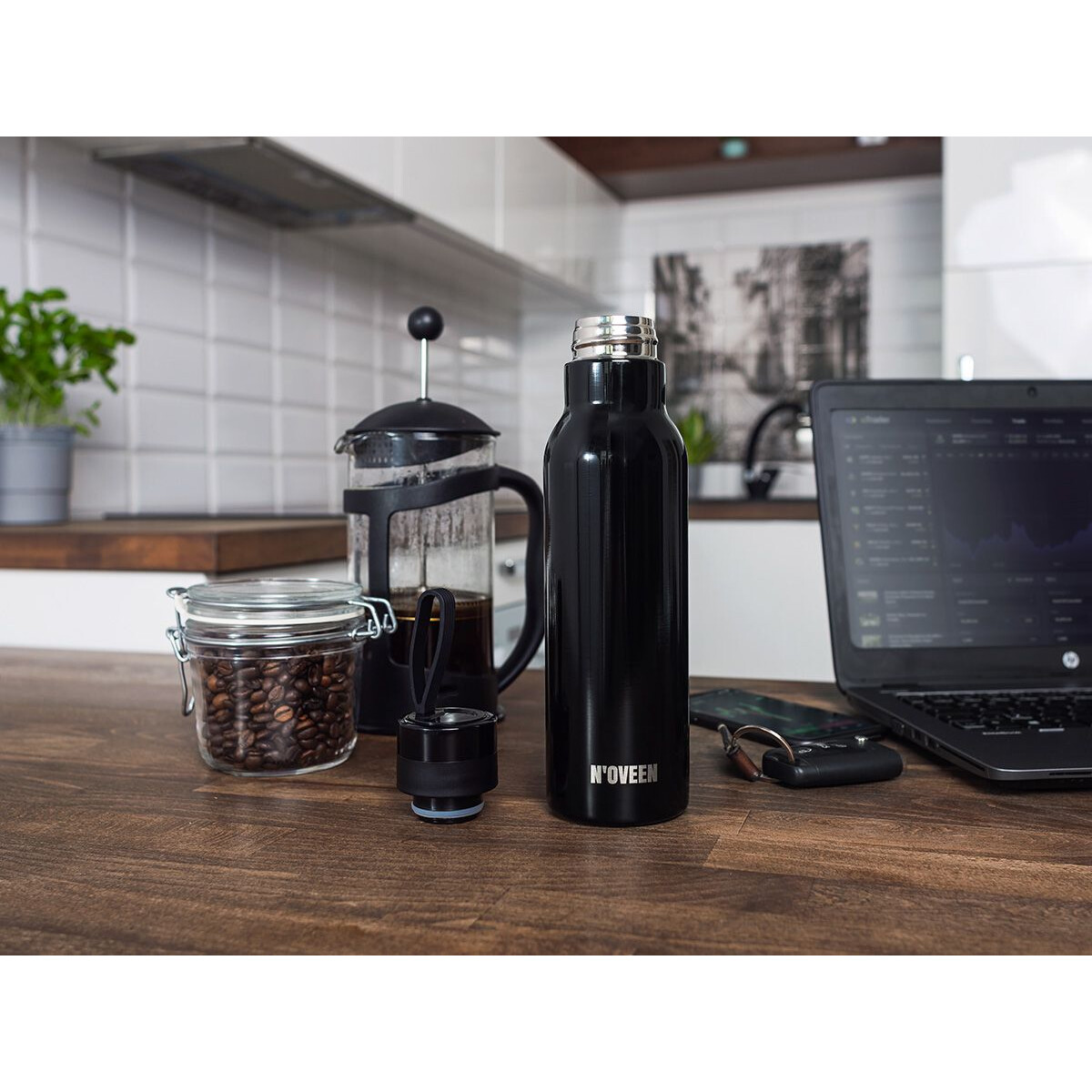 Ein Kaffee-Setup mit einer schwarzen Flasche, Kaffeebohnen, einer French Press und einem Laptop.