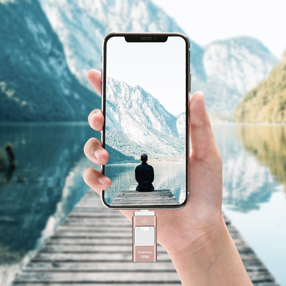 Hand, die ein Telefon mit Blick auf Berge und einen See hält, mit einem USB-Stick.