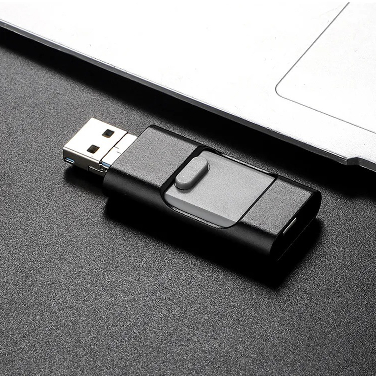 Schwarz-grauer USB-Stick auf schwarzer Oberfläche. Laptop im Hintergrund.