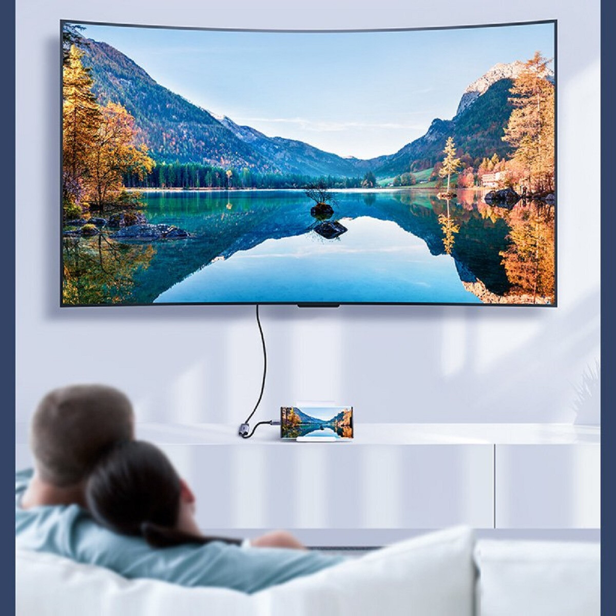Paar auf dem Sofa schaut TV mit Landschaftsbild. Ein Telefon zeigt das gleiche Bild, verbunden mit dem TV.