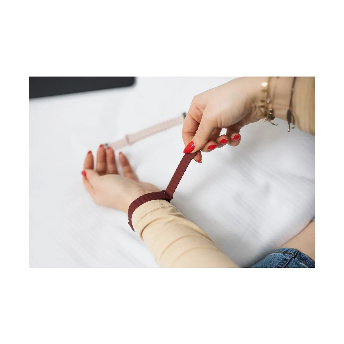 Hand hält ein weinrotes Armband über den anderen Arm.