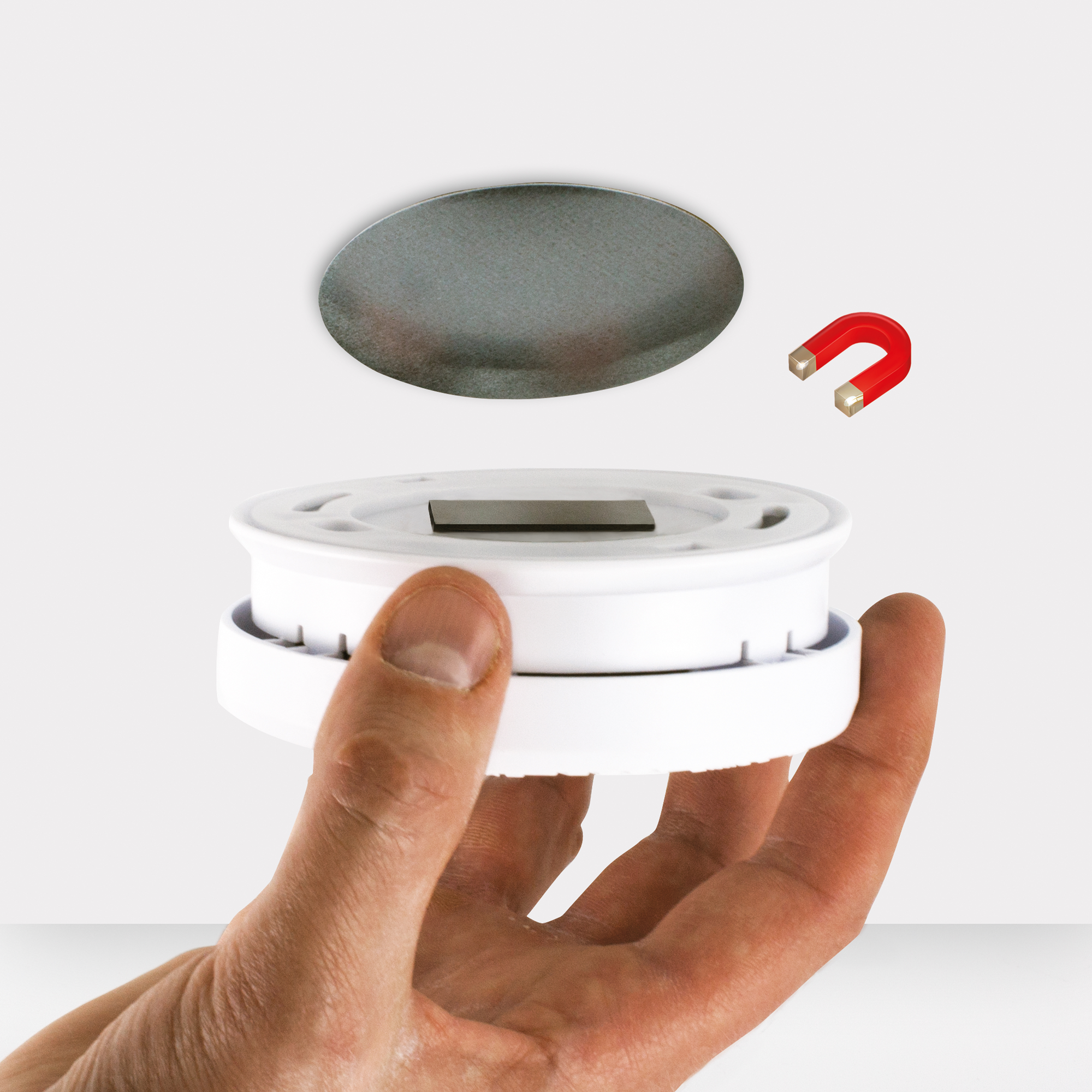 Una mano che tiene un dispositivo circolare bianco sopra una superficie bianca con un magnete.